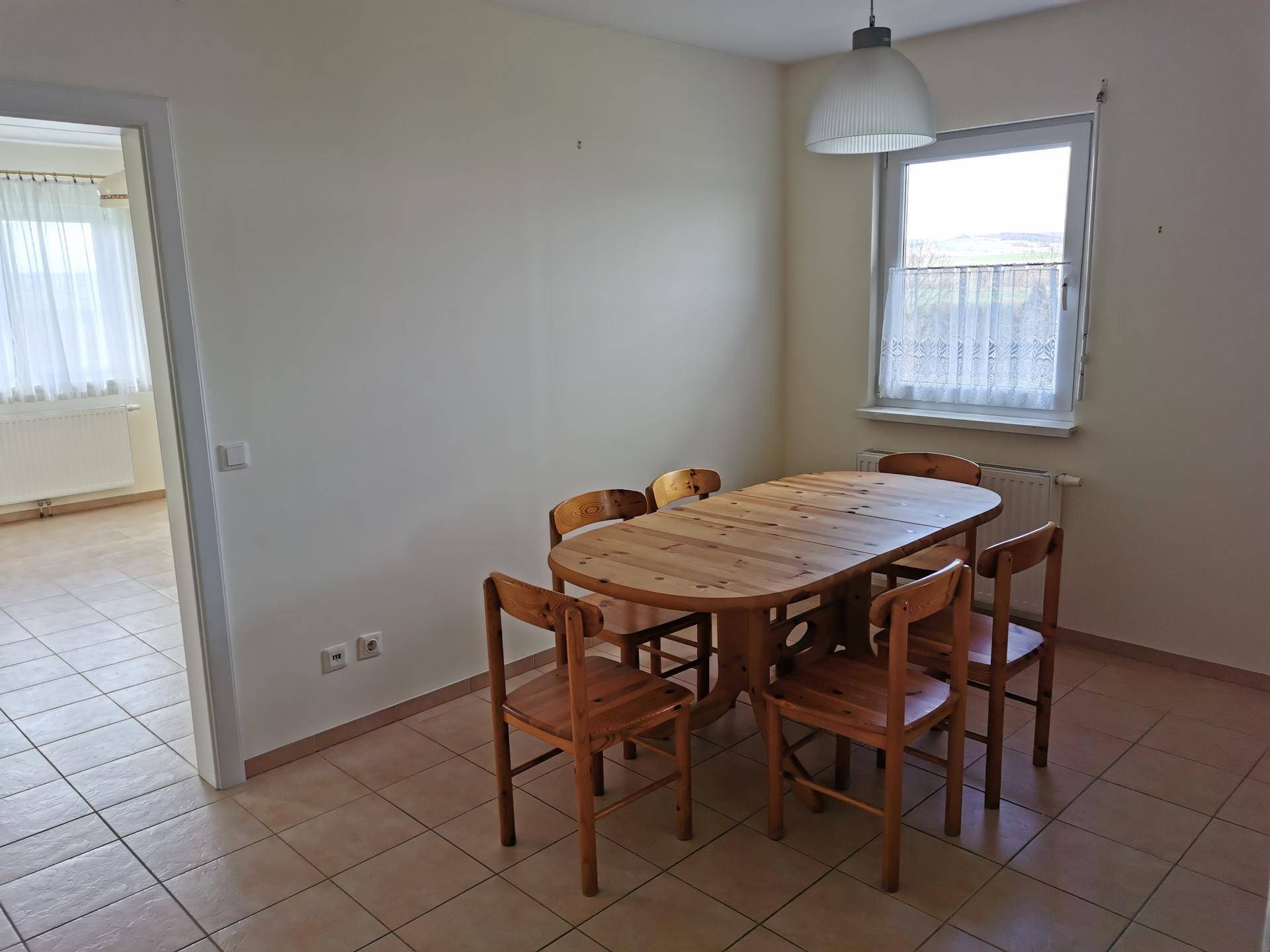 Essbereich mit rustikalem Holztisch und Stühlen, Fenster und Fliesenboden.