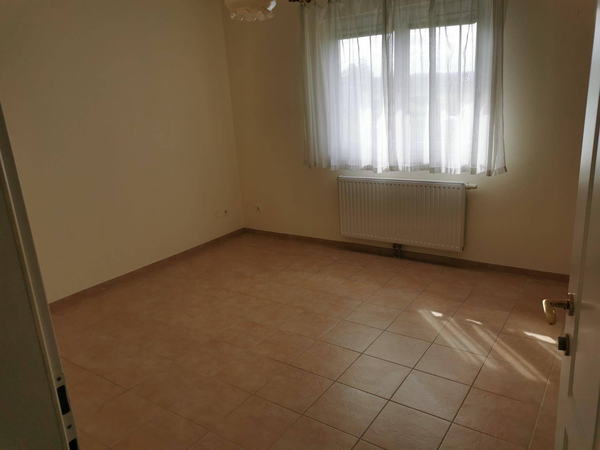 Schlafzimmer mit Fliesenboden, Fenster und Heizkörper, ideal für ein Kinderzimmer.