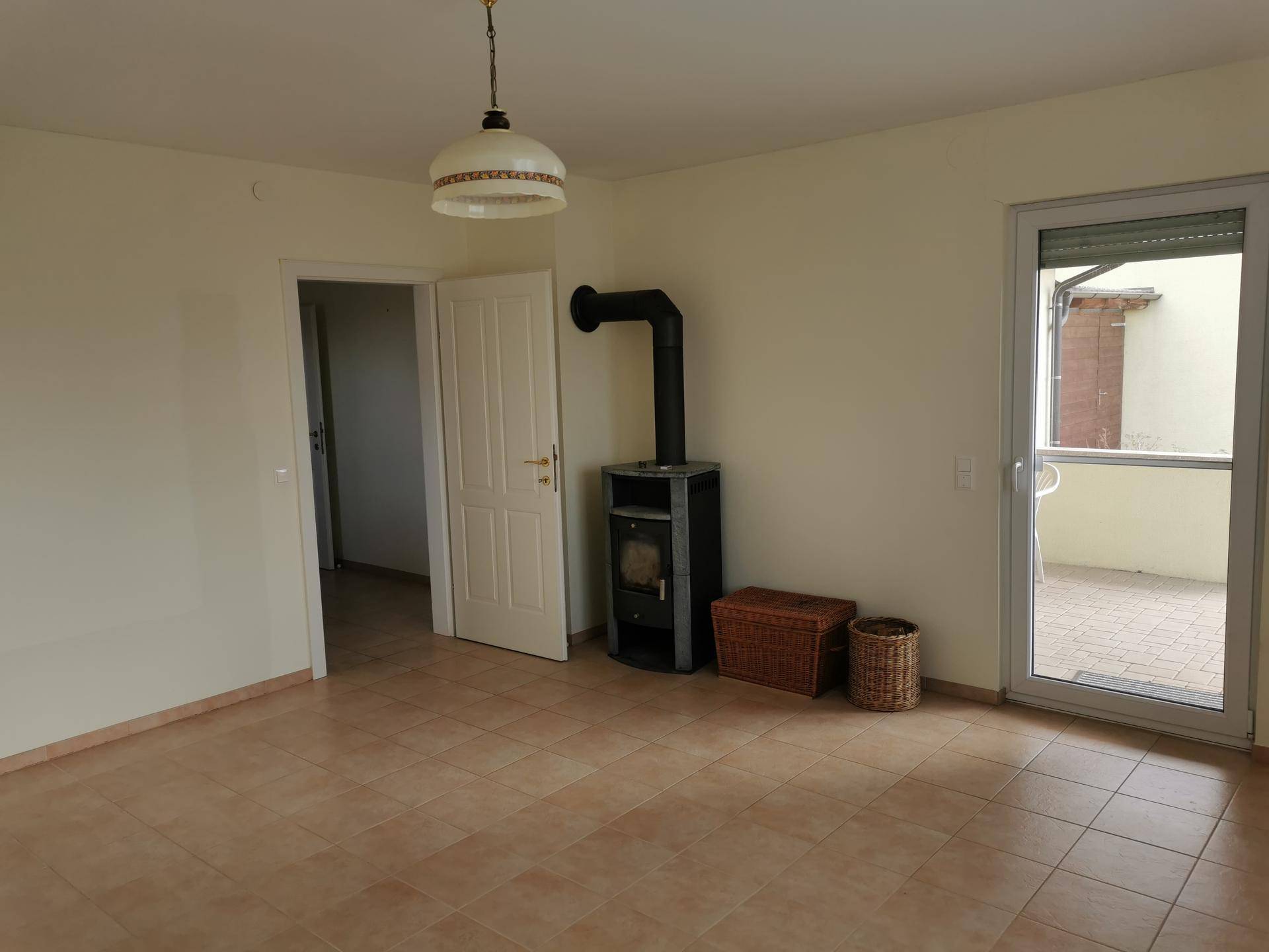 Helles Wohnzimmer mit Kaminofen, Fliesenboden und Zugang zur Terrasse.