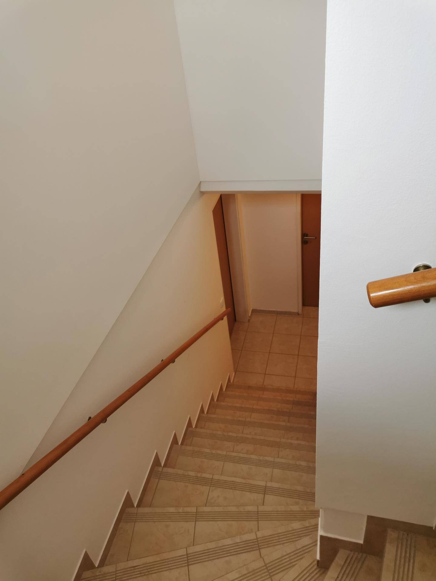 Treppenhaus mit Holzgeländer und Fliesenstufen, das in das Untergeschoss führt.