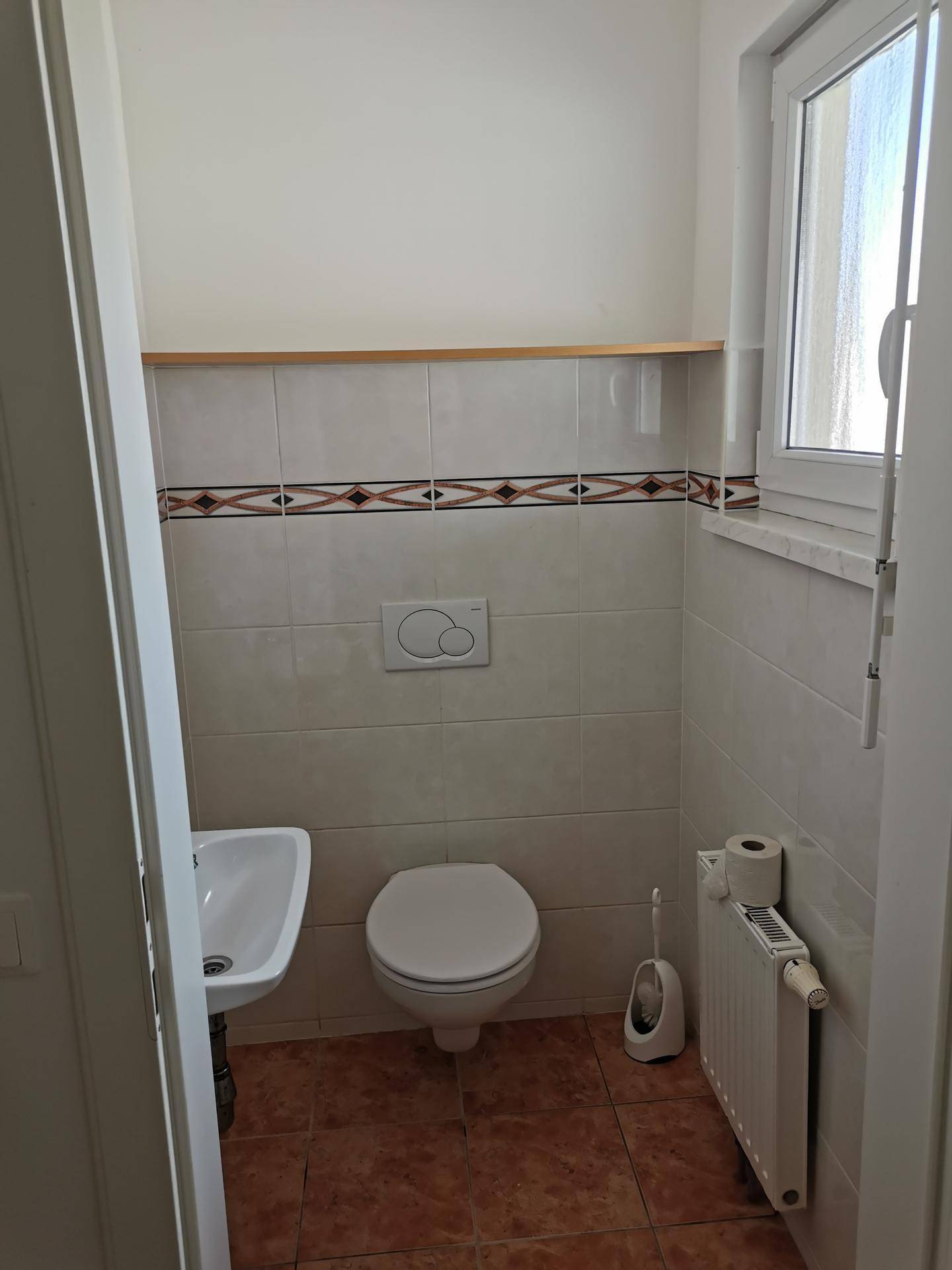Kleines Gäste-WC mit Wand-WC, Waschbecken, Fenster und gemusterten Fliesenbordüren.
