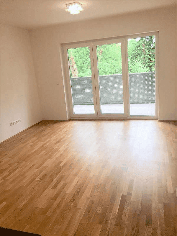 Helles Schlafzimmer mit Holzboden und Zugang zu einem Balkon, ideal für natürliche Belüftung.