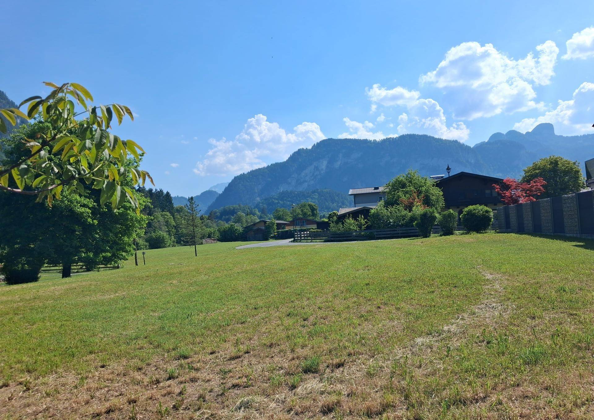 Sonnige Wiese mit Blick auf die umliegenden Berge und vereinzelte Häuser in der Ferne.