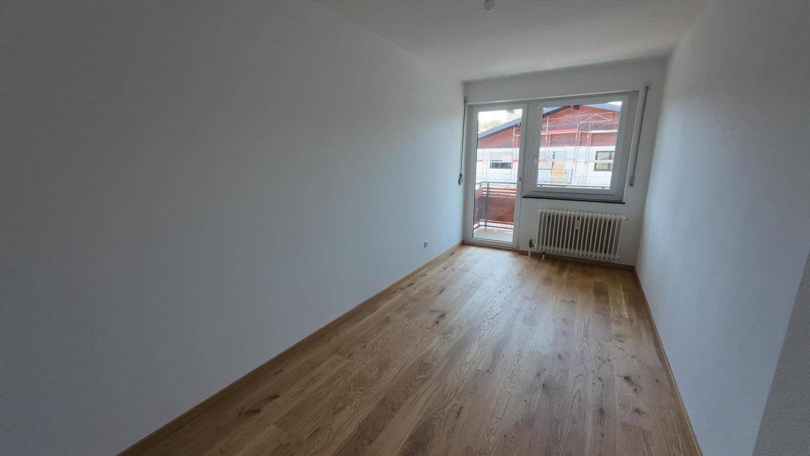 Schlafzimmer mit Holzboden und Zugang zu einem kleinen Balkon, der viel Licht hereinlässt.