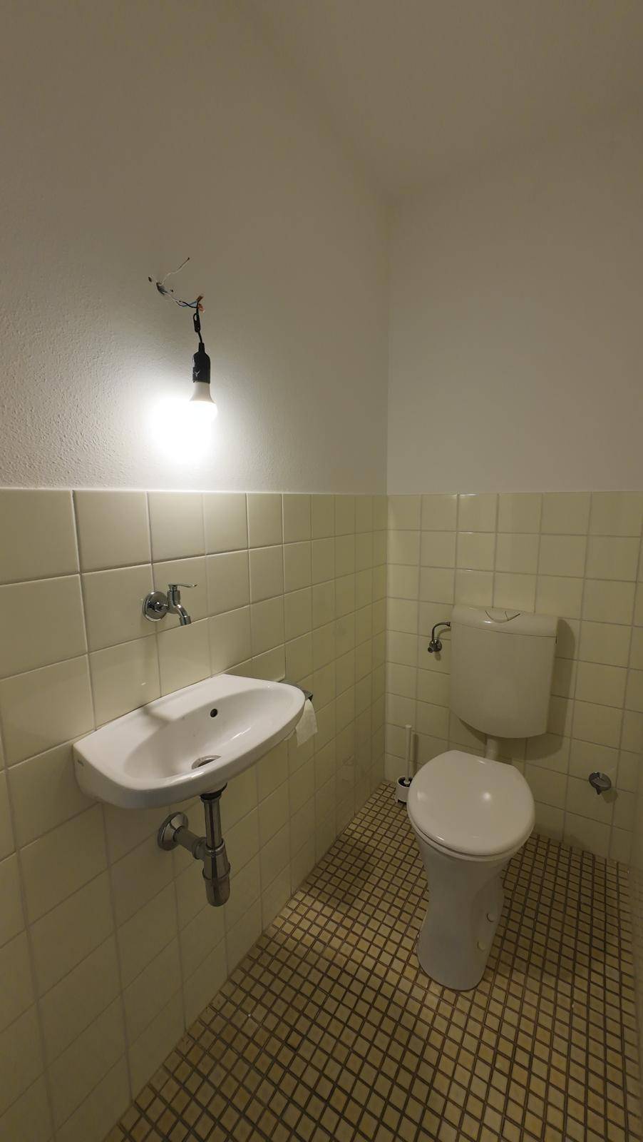Kleines Gäste-WC mit hellen Fliesen, Waschbecken und Toilette.