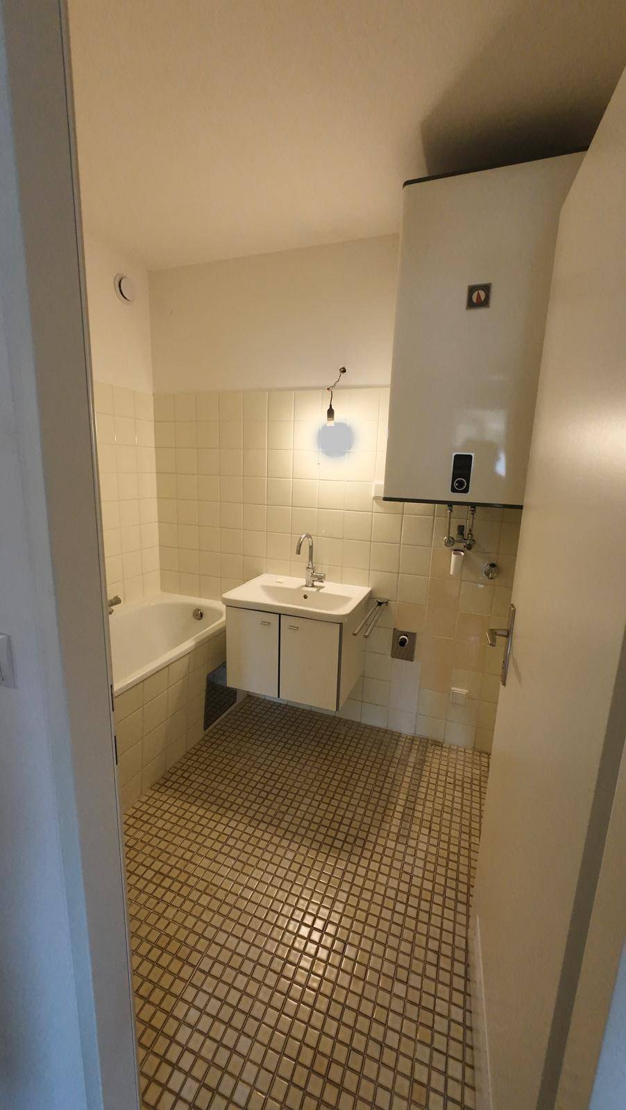 Badezimmer mit Badewanne, Waschbecken und Wandboiler, ausgestattet mit hellen Fliesen.