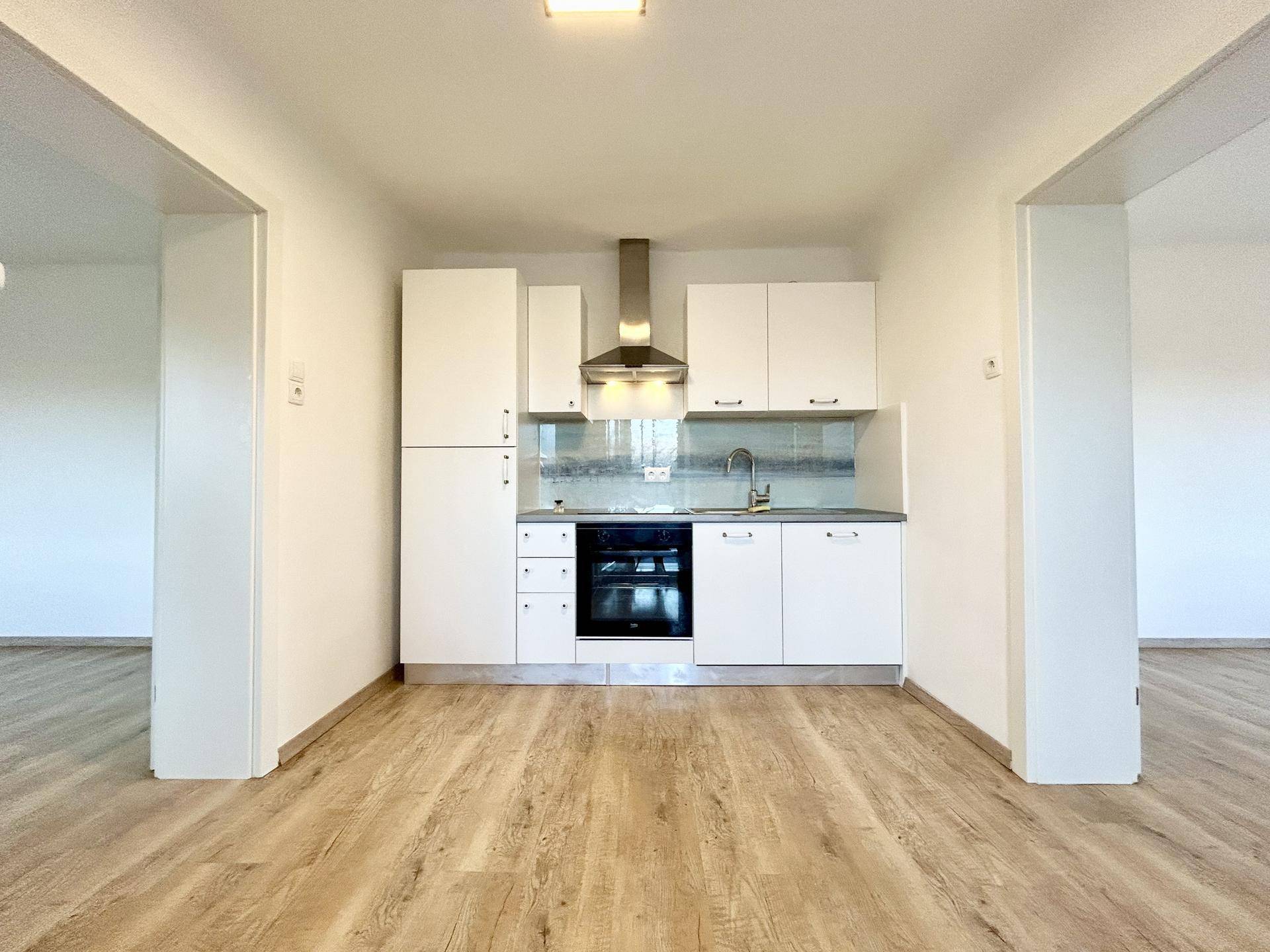 Kleine, moderne Einbauküche mit weißen Schränken, integriertem Backofen und Dunstabzugshaube.
