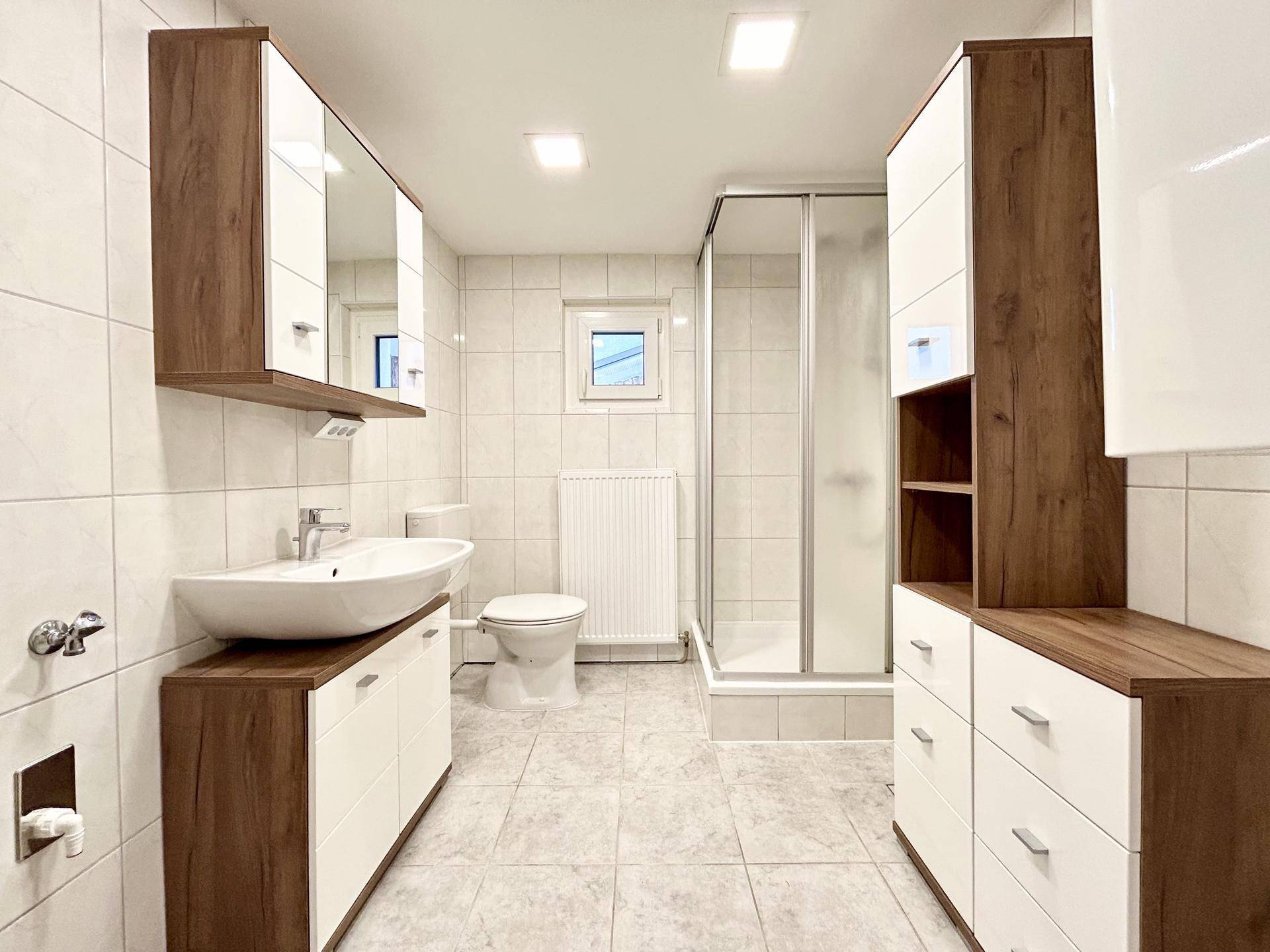 Modernes Badezimmer mit Duschkabine, Waschtisch, WC und Spiegelschrank, hell gefliest.