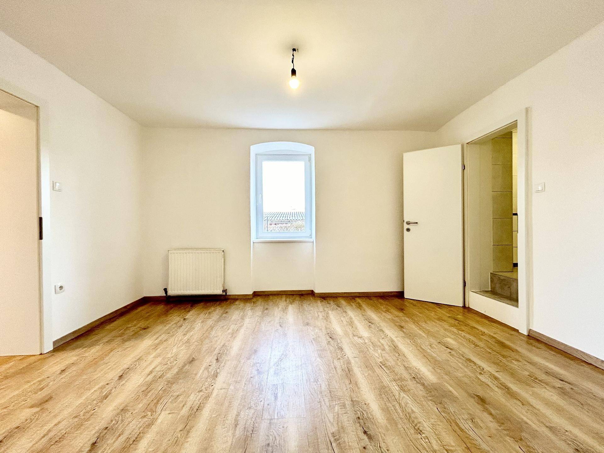 Leerer Raum mit Holzboden, weiß gestrichenen Wänden und einem Fenster, bereit zur individuellen Gestaltung.