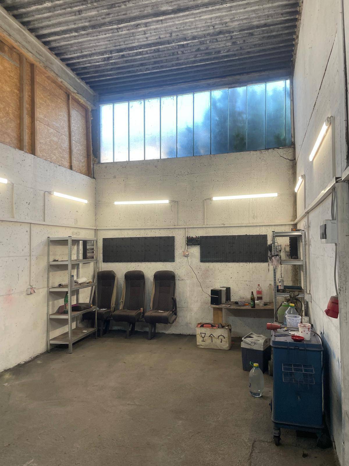 Großer Werkstattbereich mit Metallregalen, Sitzgelegenheiten und hohen Fenstern für Tageslicht.