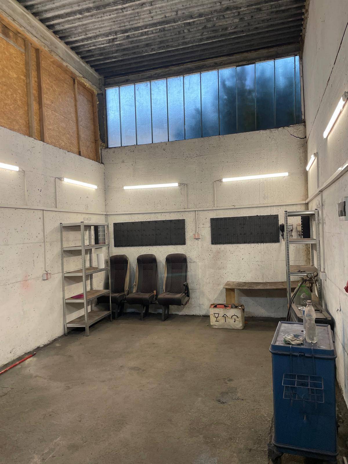 Großer Werkstattbereich mit Metallregalen, Sitzgelegenheiten und hohen Fenstern für Tageslicht.