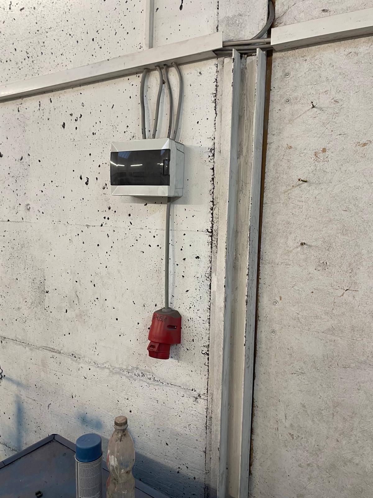 Nahaufnahme einer elektrischen Verteilung und roten Industriesteckdose an der Betonwand.