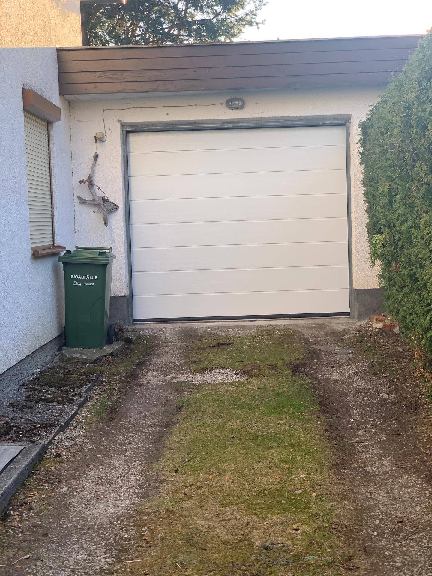 Weiße Garagentür und teilweise schneebedeckte Einfahrt mit einem Mülleimer.
