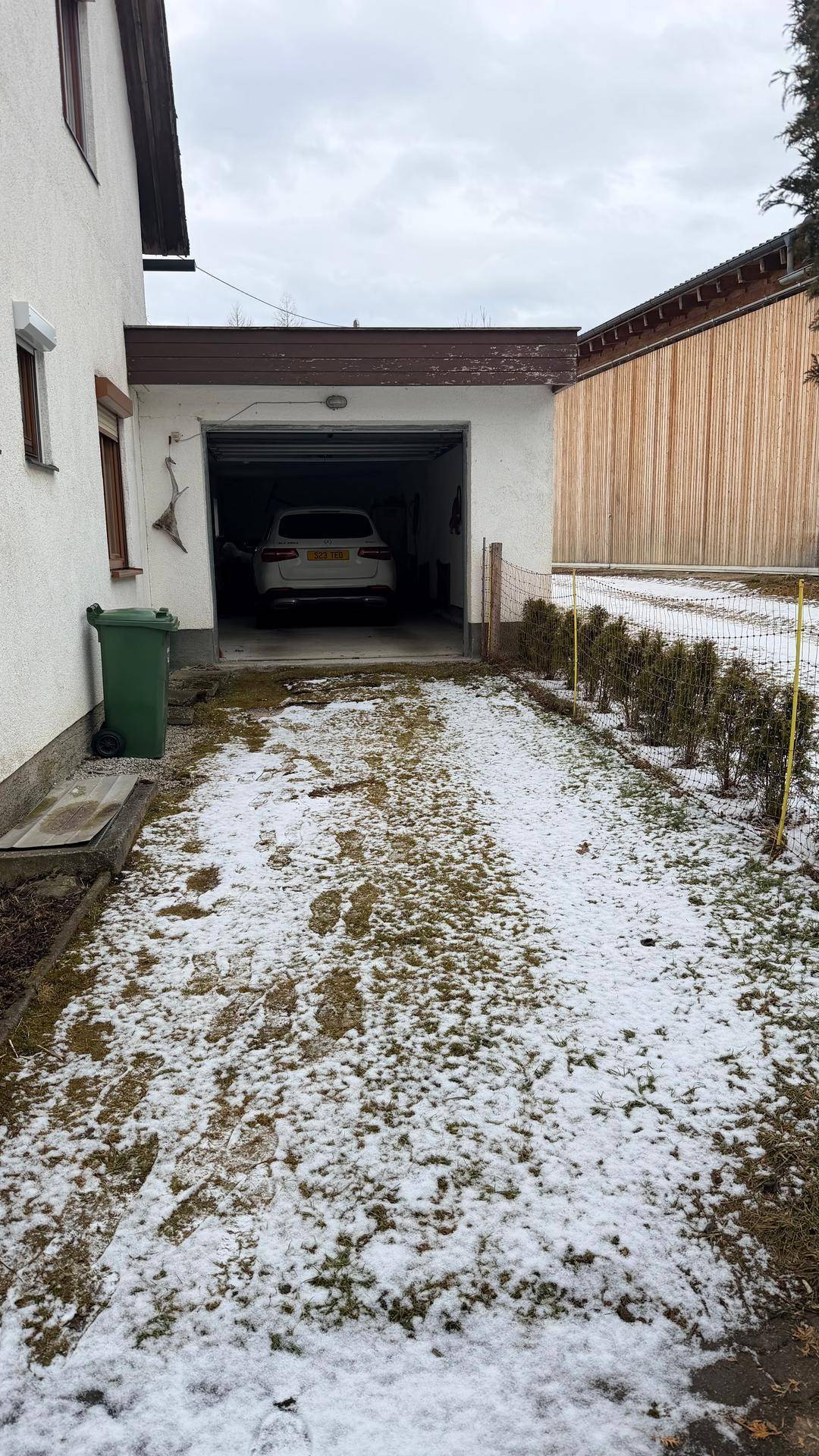 Einfahrt zum offenen Garagenbereich mit einem geparkten Auto auf schneebedecktem Boden.