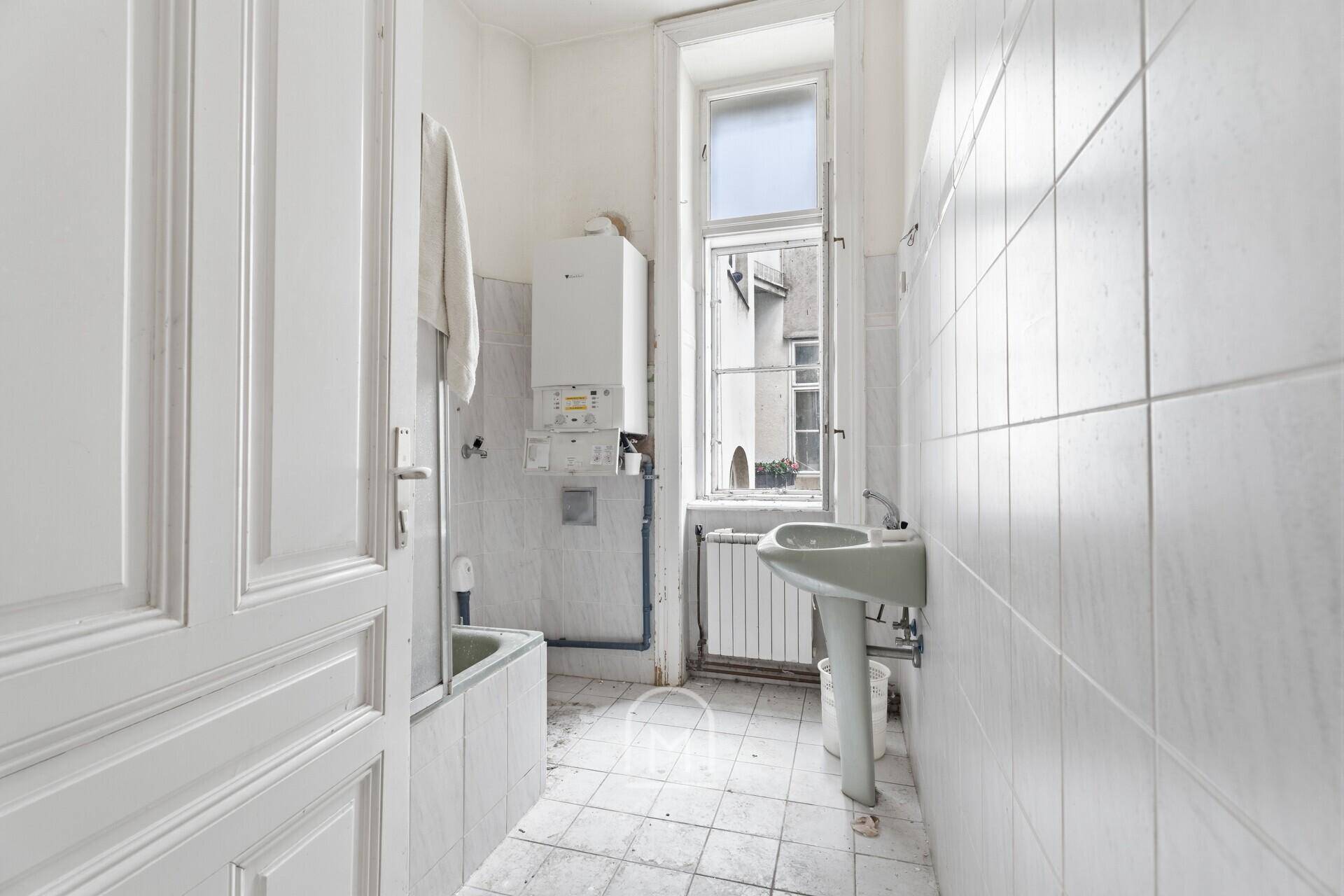 Badezimmer mit Badewanne, Waschbecken und Fenster, das eine Renovierung benötigt.