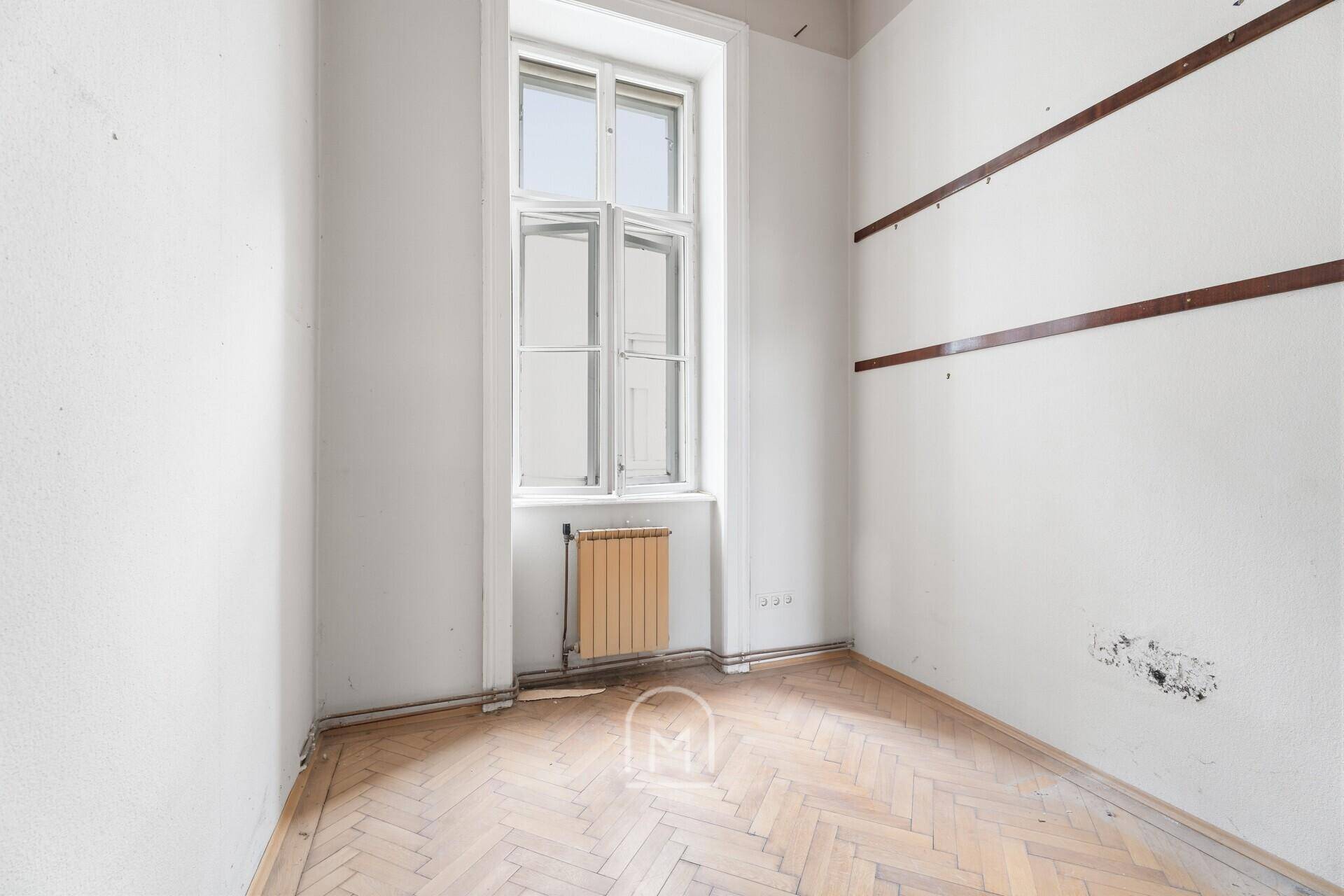 Kleines Zimmer mit Fischgrätparkett und einem Fenster, das auf den Innenhof blickt.