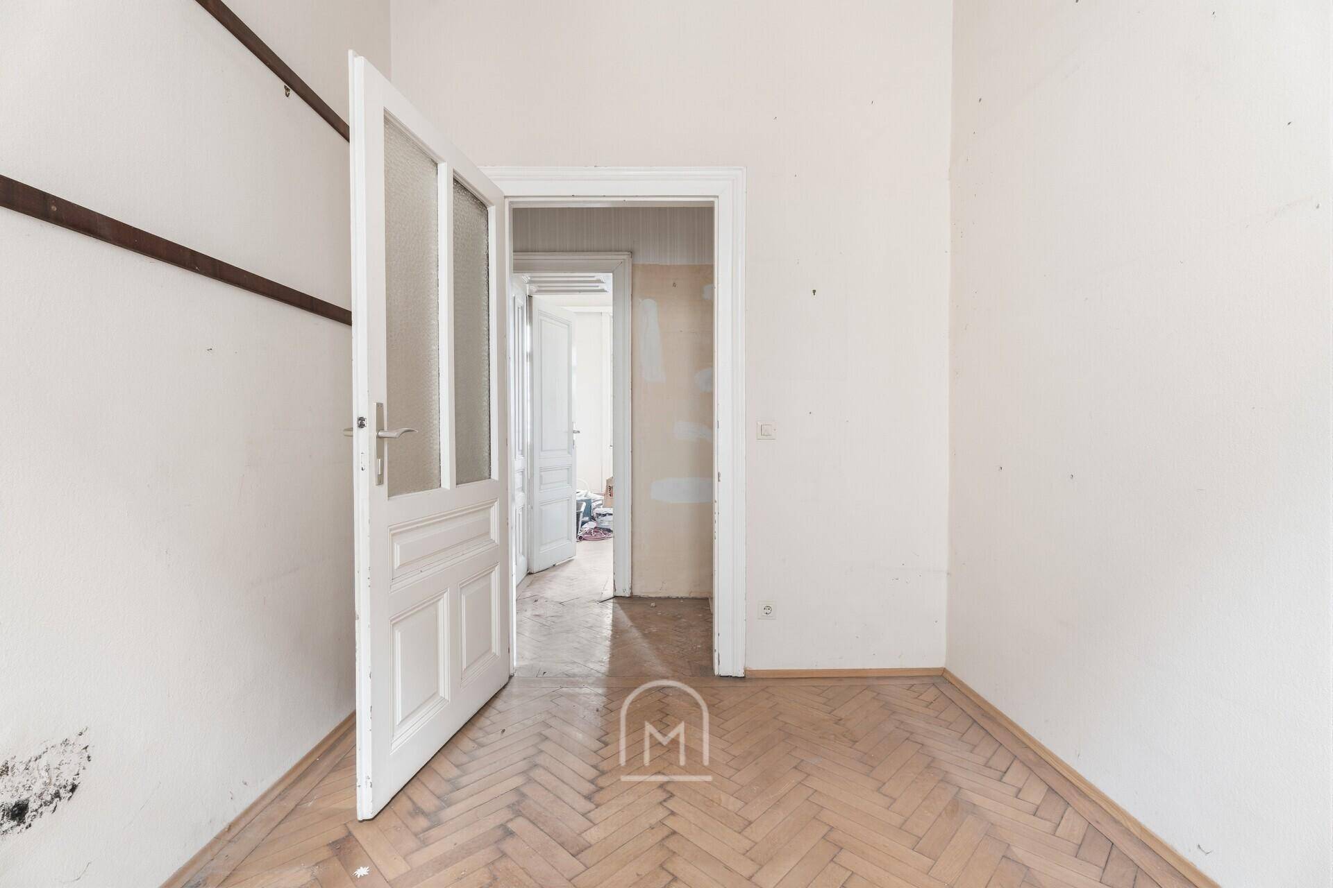 Helles kleines Zimmer mit Fischgrätparkett und einer Tür, die zu weiteren Räumen führt.