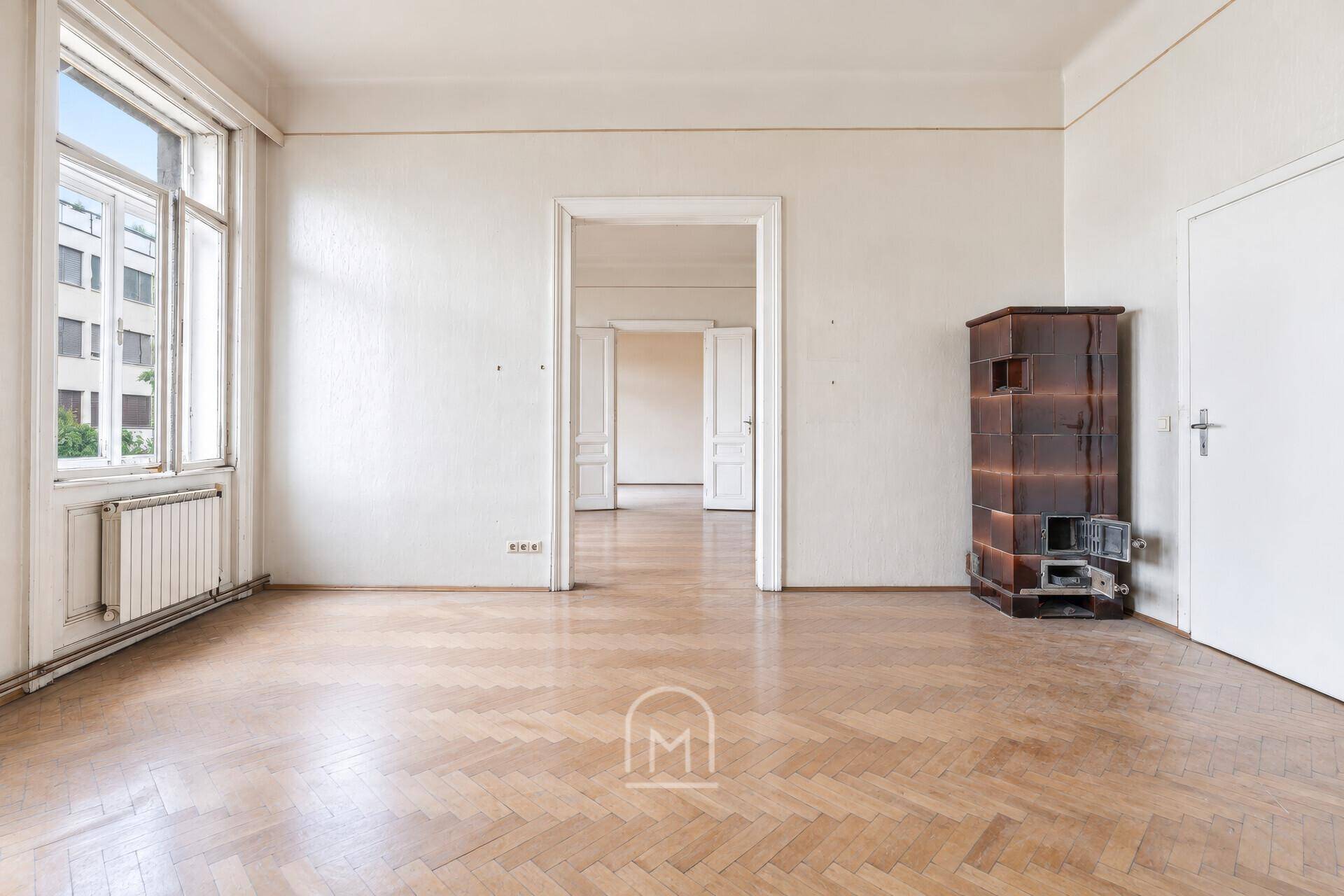 Großes Zimmer mit Fischgrätparkett und einem traditionellen Kachelofen, der Wärme spendet.