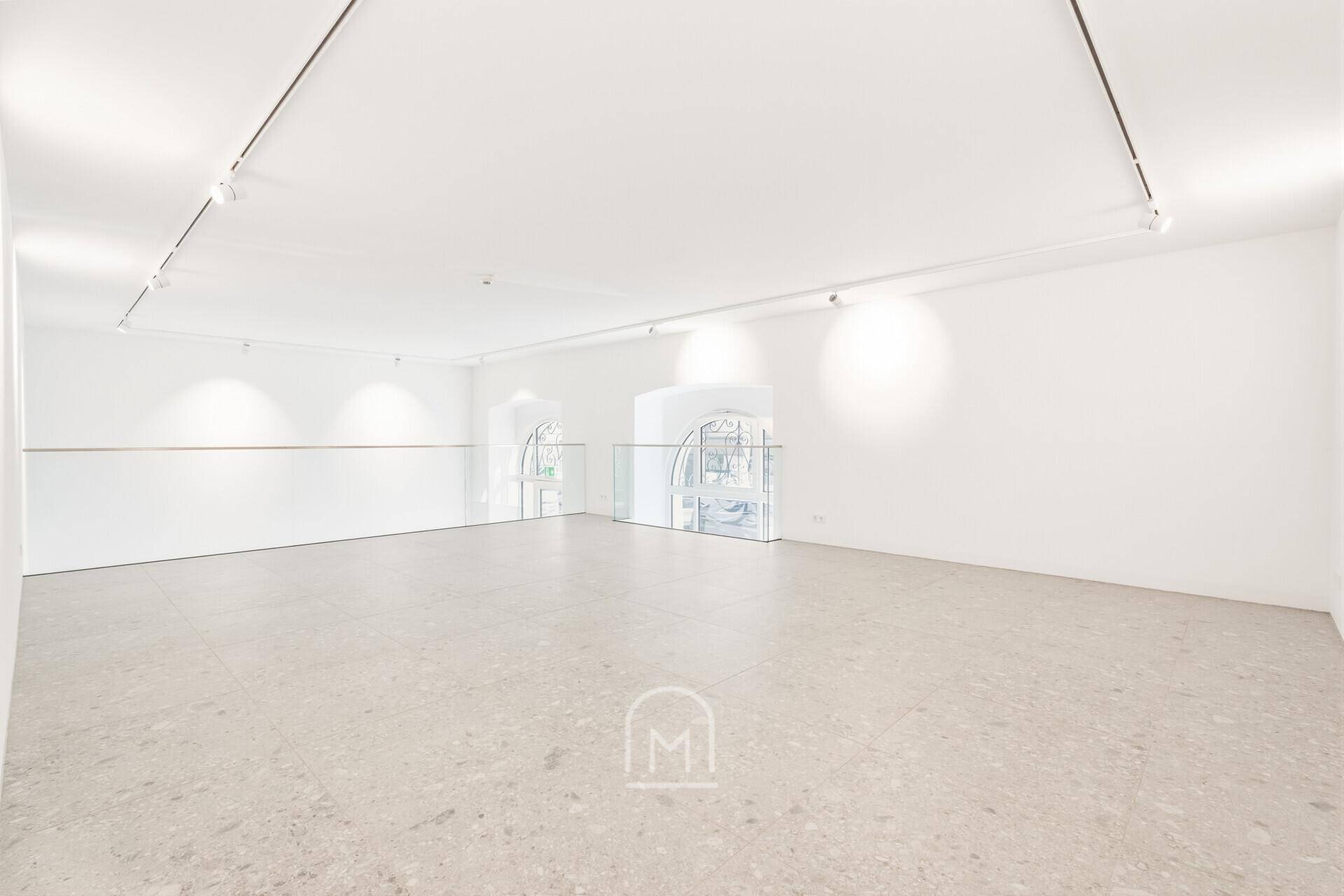 Offene Galerie mit Blick durch ein großes Bogenfenster und moderner Glasbrüstung.