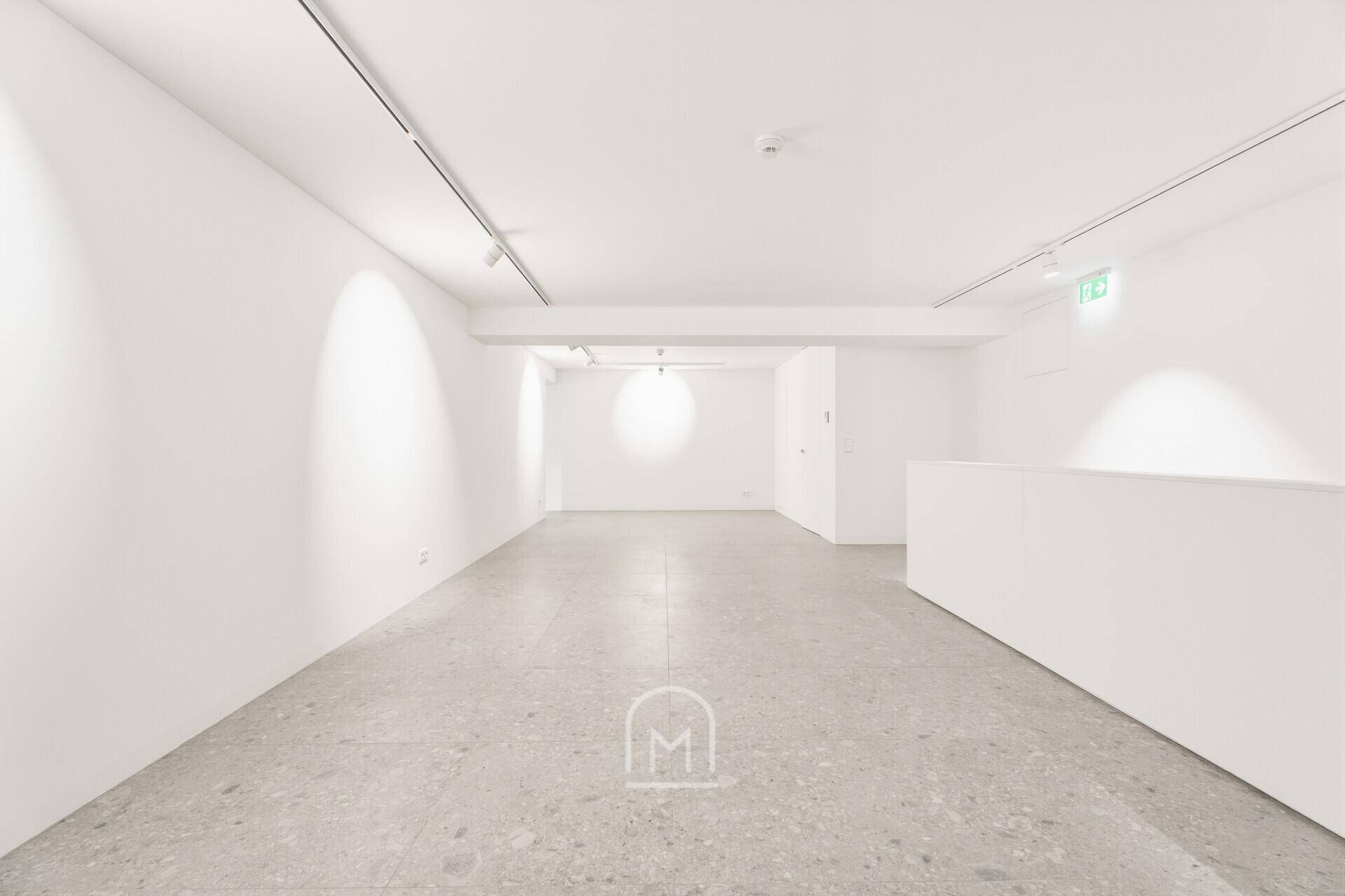 Langer, heller Galerieraum mit weiß gestrichenen Wänden und moderner Beleuchtung.