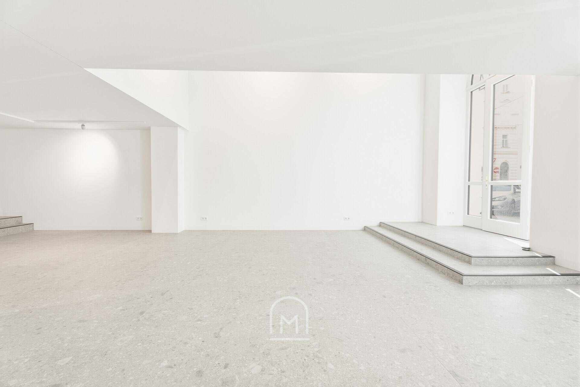 Großer, leerer Gewerberaum mit weiß gestrichenen Wänden und elegantem Steinboden.