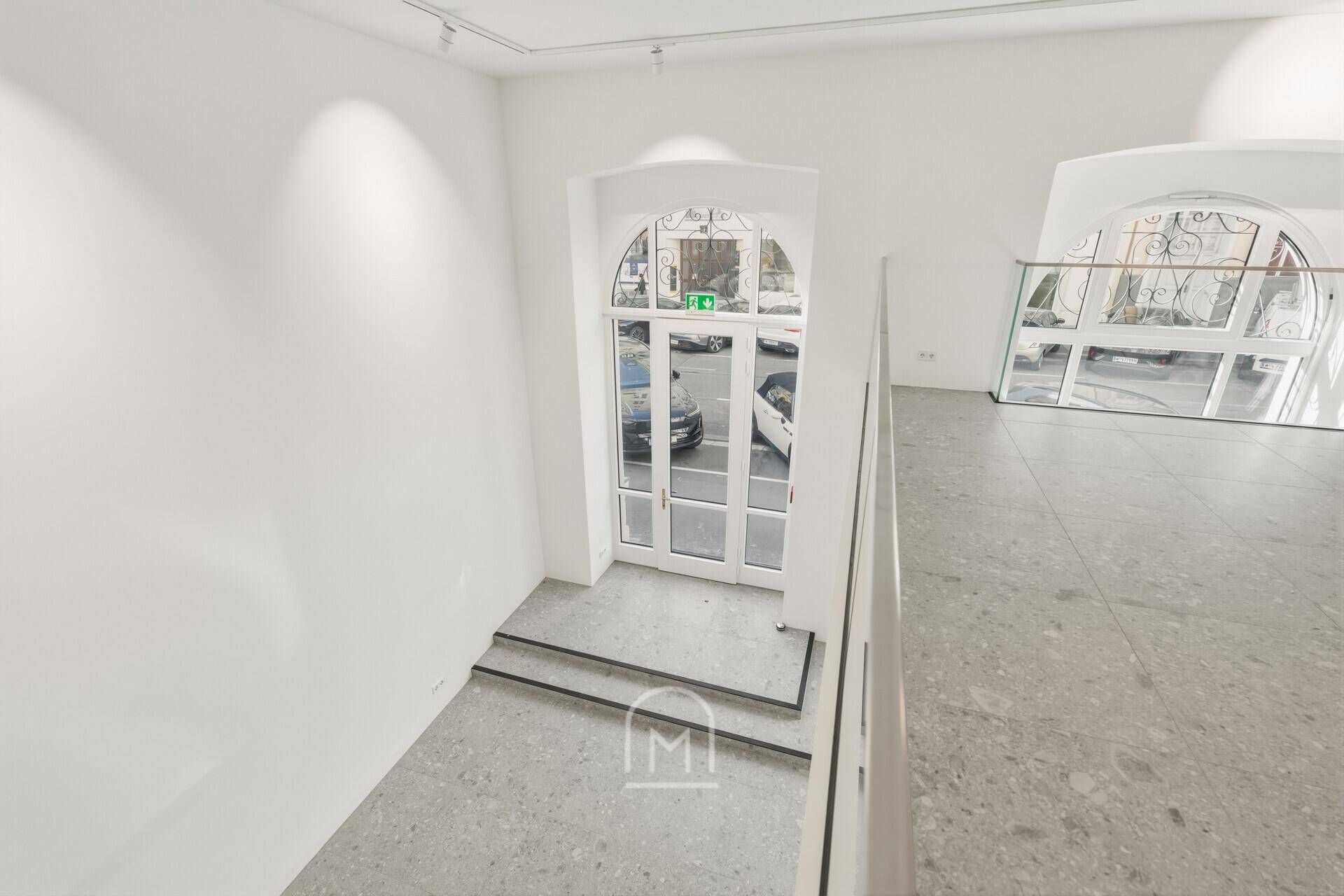 Blick von der Galerie auf den Eingangsbereich mit großen Bogenfenstern und Treppenaufgang.