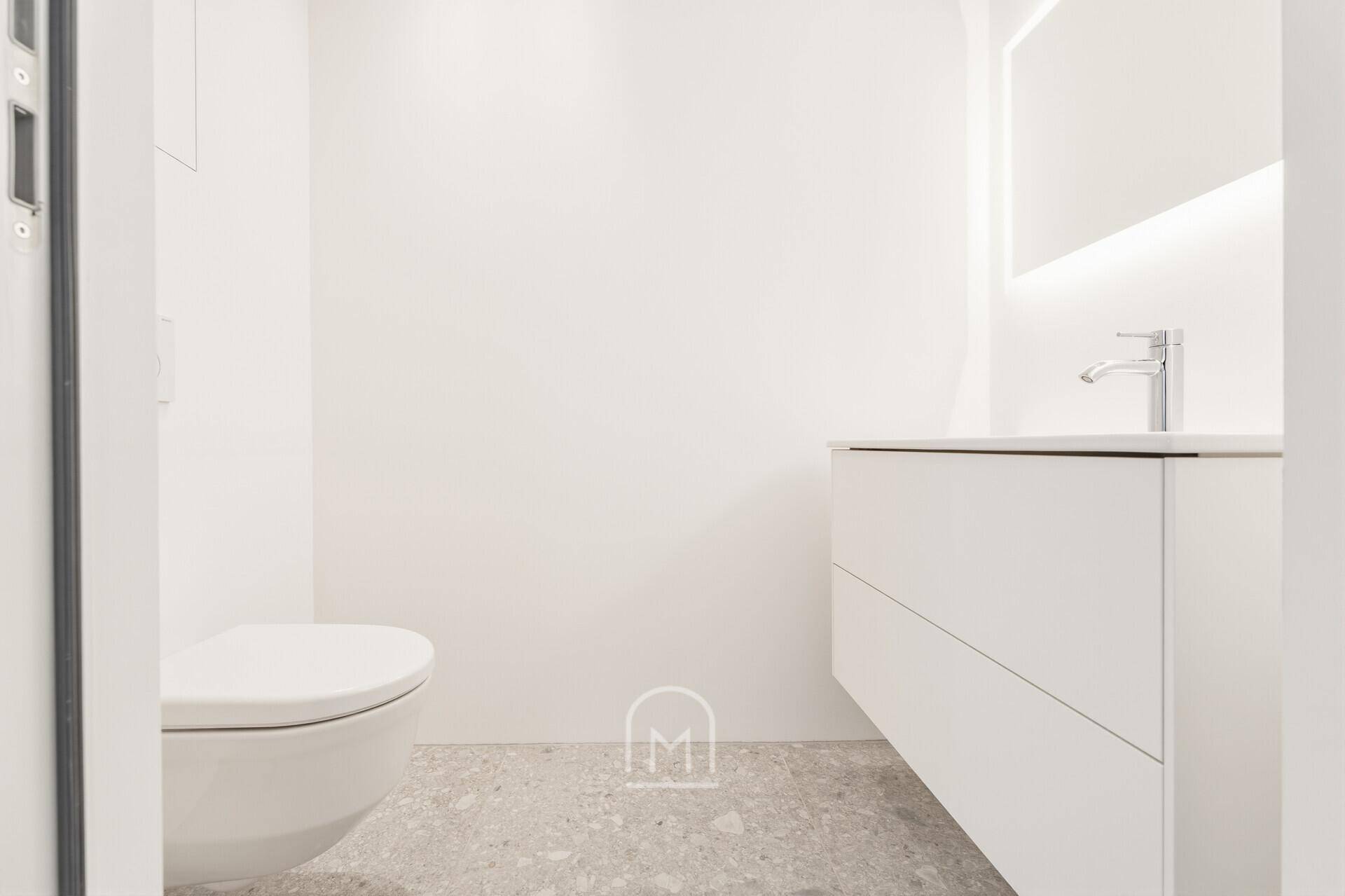 Modernes WC mit wandhängender Toilette, schwebendem Waschtisch und beleuchtetem Spiegel.
