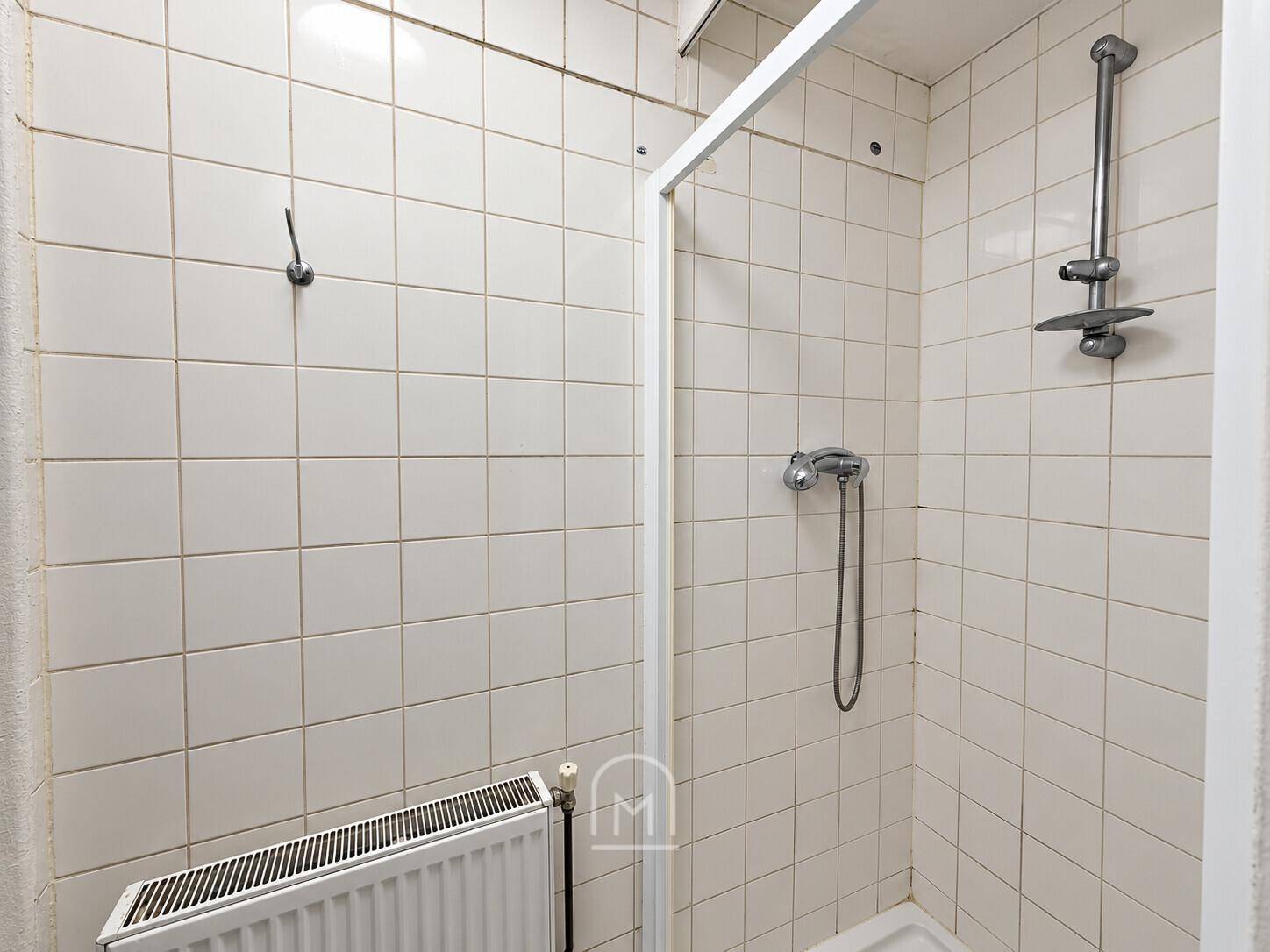 Geflieste Duschkabine mit Heizkörper und einfacher Ausstattung.