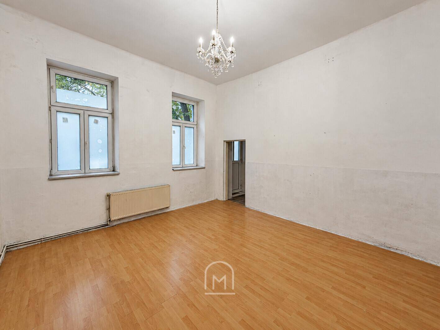Leeres Zimmer mit Laminatboden, hohen Decken und Blick nach draußen.