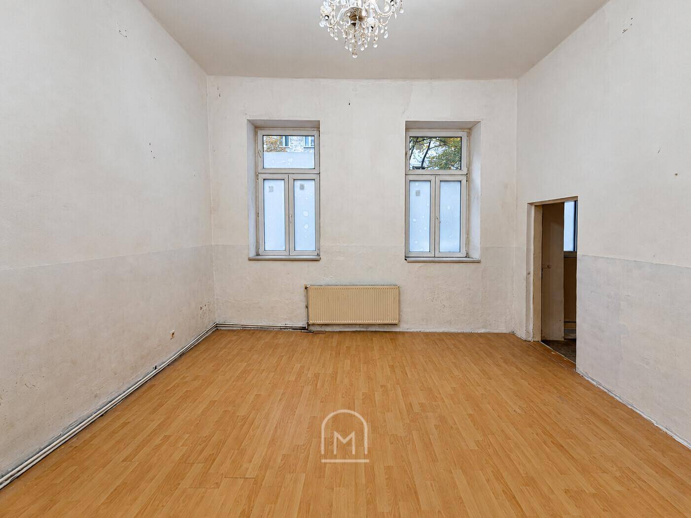 Helles Zimmer mit Laminatboden, Kronleuchter und schlichten Wänden.