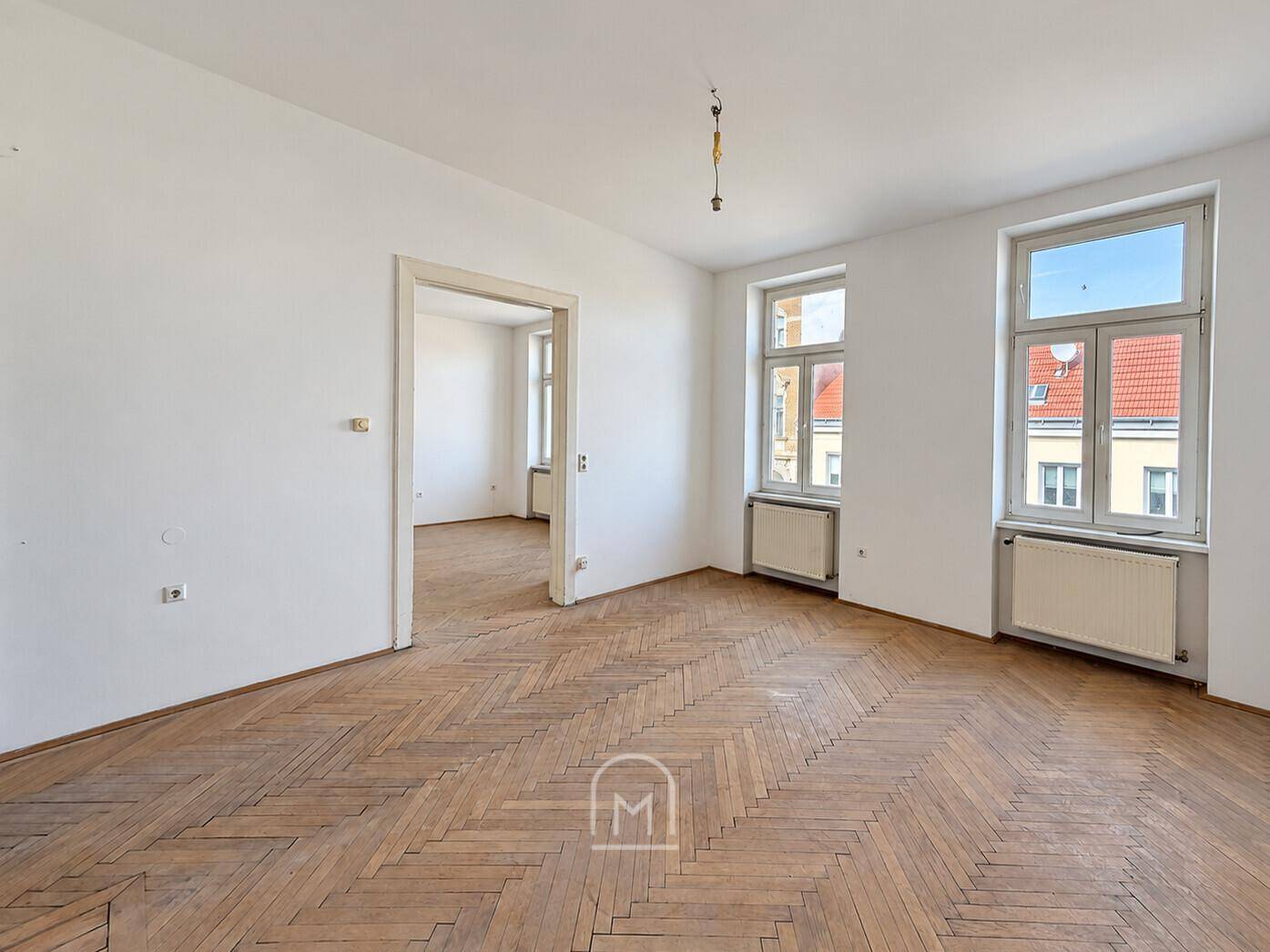Helles Zimmer mit Fischgrätparkett und Zugang zu einem weiteren Raum, ideal für offene Wohnkonzepte.