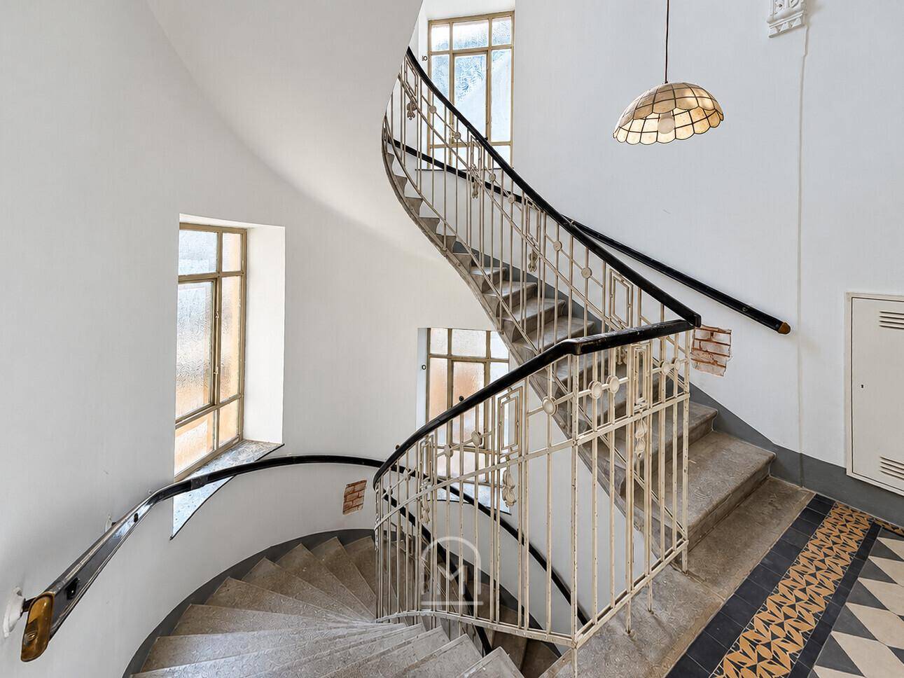 Elegantes Treppenhaus mit geschwungener Steintreppe und kunstvollem Geländer in einem Altbau.