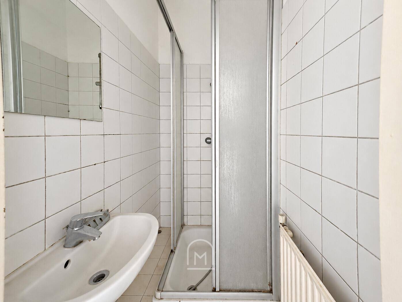 Kleines Badezimmer mit weißen Fliesen, Waschbecken und einer Duschkabine mit integrierter Wanne.
