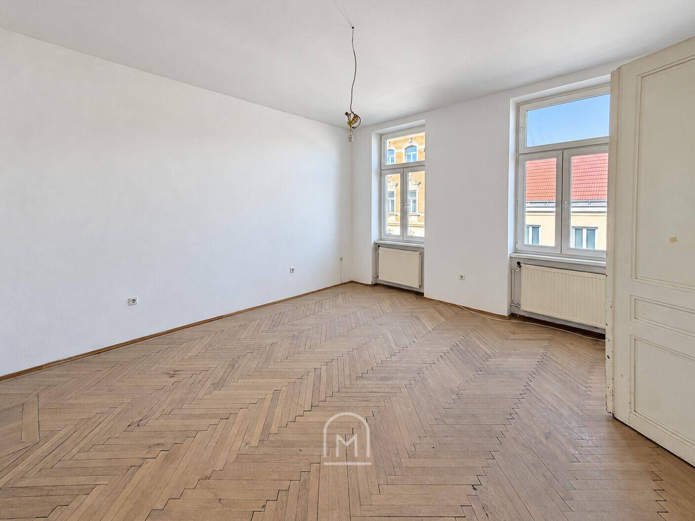 Lichtdurchflutetes Zimmer mit elegantem Fischgrätparkett und hohen Decken, bereit zur individuellen Gestaltung.