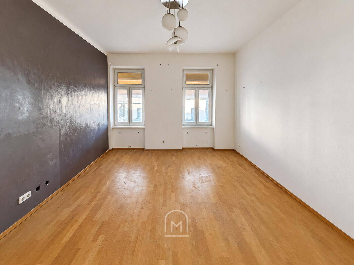 Geräumiges Zimmer mit Holzboden und einer markanten dunkelgrauen Wand, ideal für Wohnzwecke.