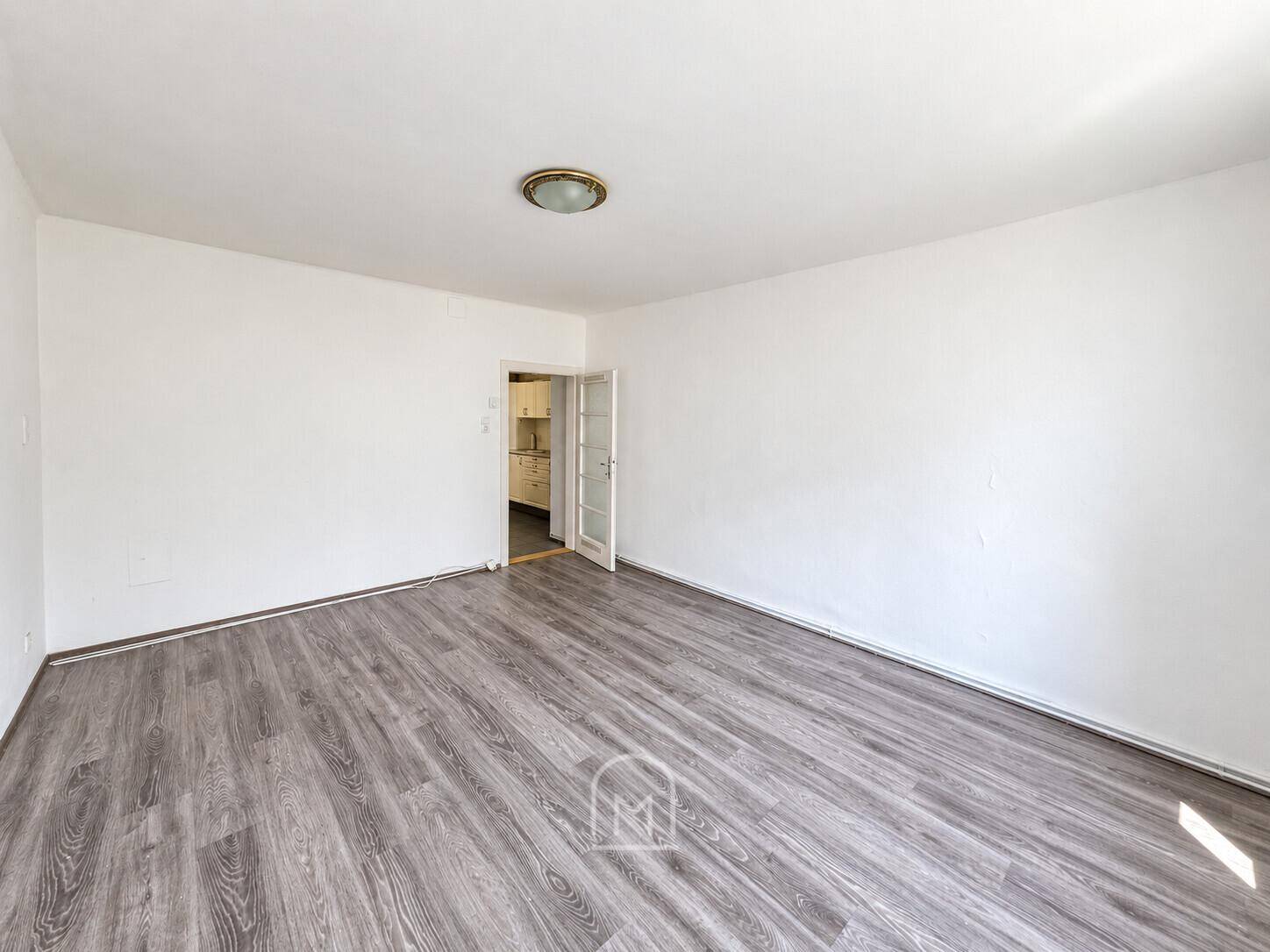 Helles Zimmer mit Laminatboden und offener Tür, die in eine angrenzende Küche führt.