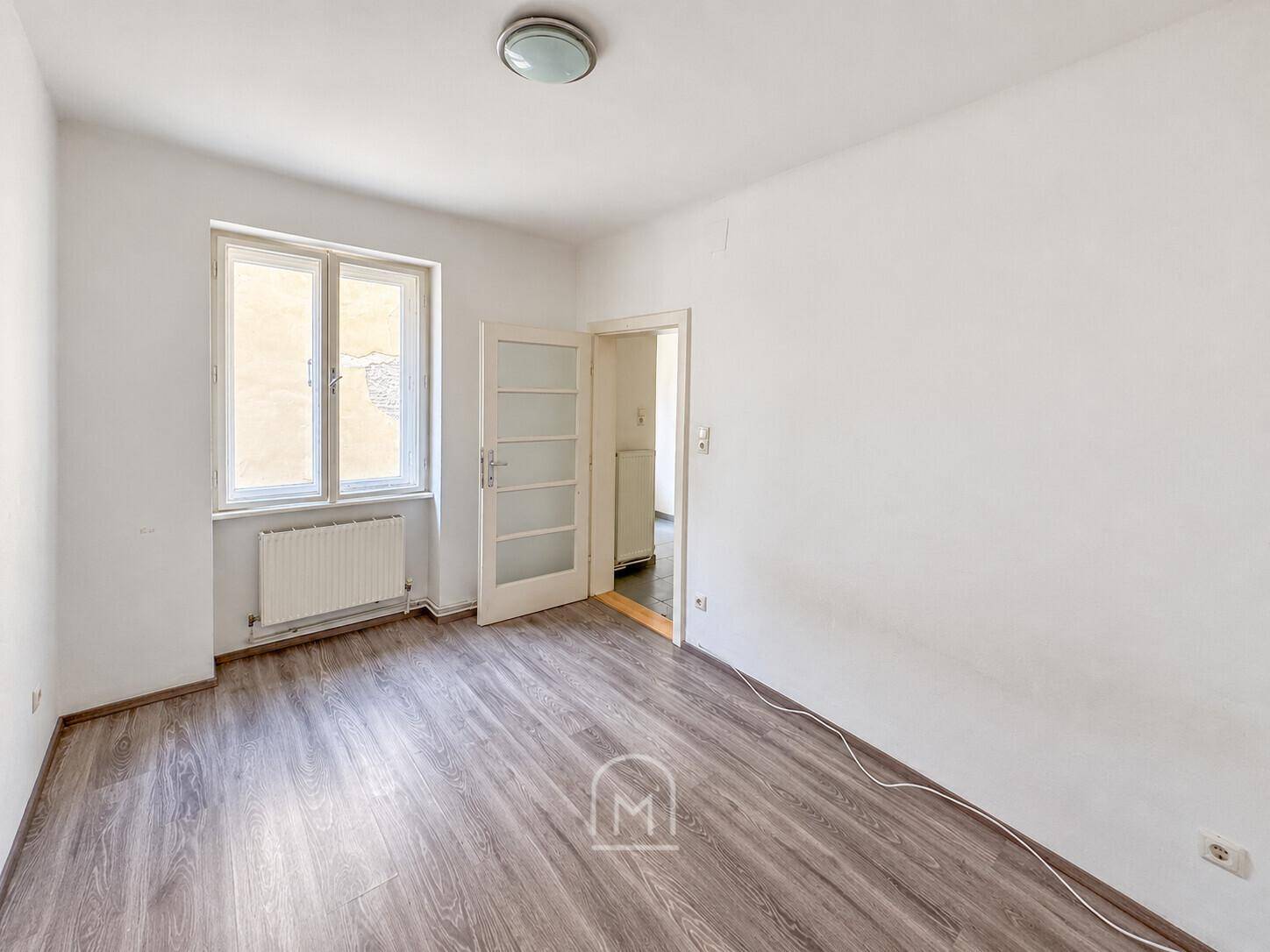 Geräumiges Zimmer mit Laminatboden, weißen Wänden und einer Tür mit Glaseinsätzen.