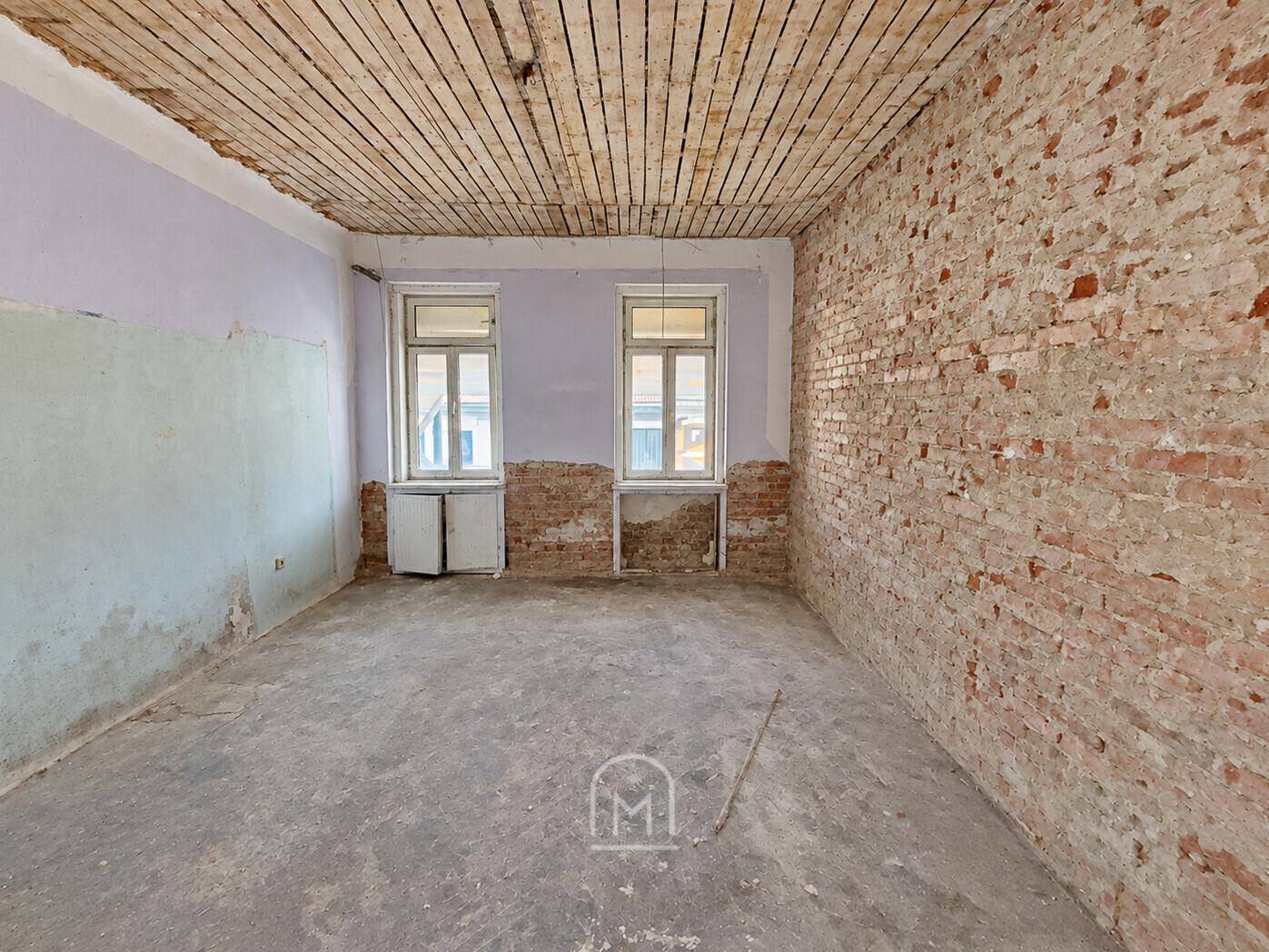 Geräumiger Raum im Rohzustand mit sichtbaren Ziegeln und Holzdecke, ideal für individuelle Gestaltung.