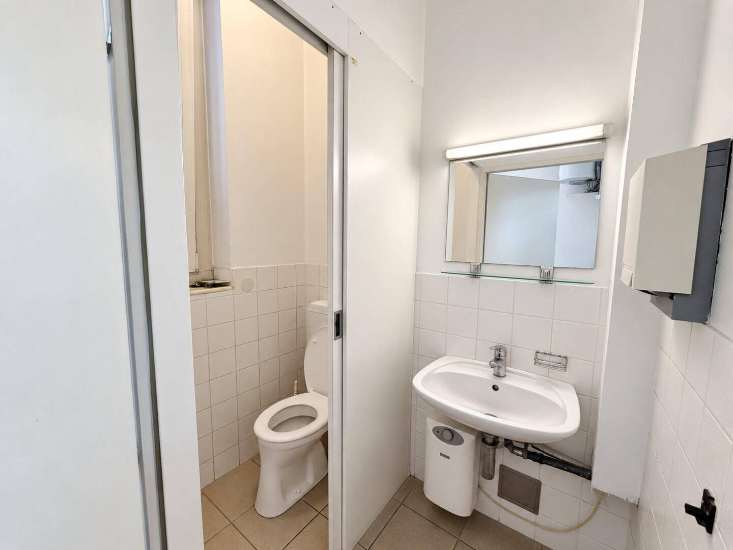 Kleiner Toilettenraum mit Waschbecken, Spiegel und WC, ausgestattet mit hellen Fliesen.