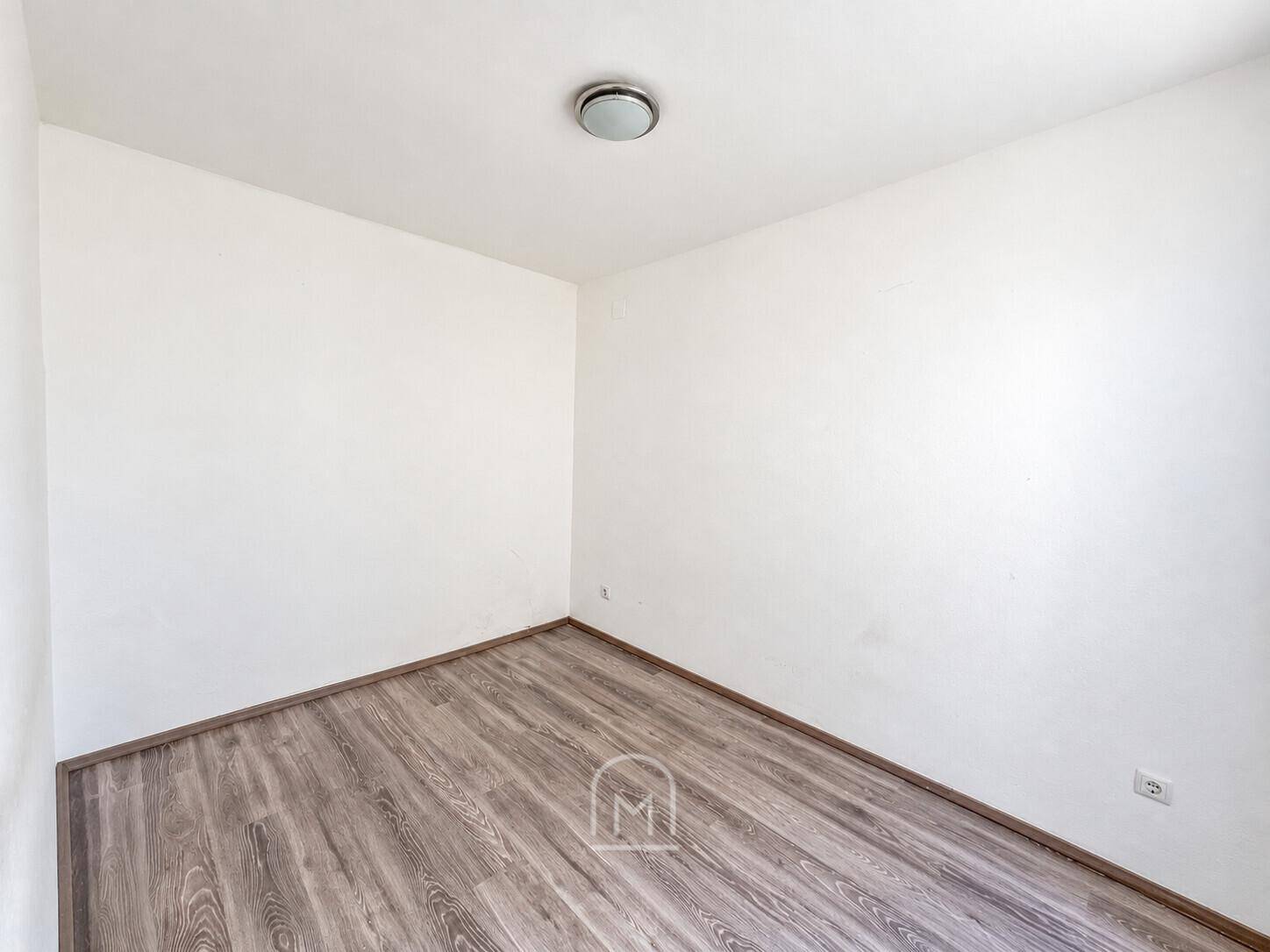 Leerer Raum mit Laminatboden und weißen Wänden, bereit zur individuellen Gestaltung.