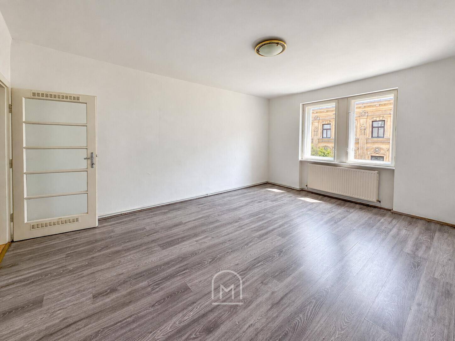 Geräumiges Zimmer mit hellem Laminatboden und Fensterblick auf die Stadt.