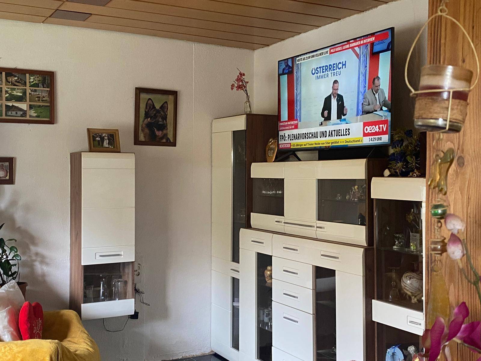 Gemütliches Wohnzimmer mit Fernseher, modernen Schränken und gelbem Sessel.