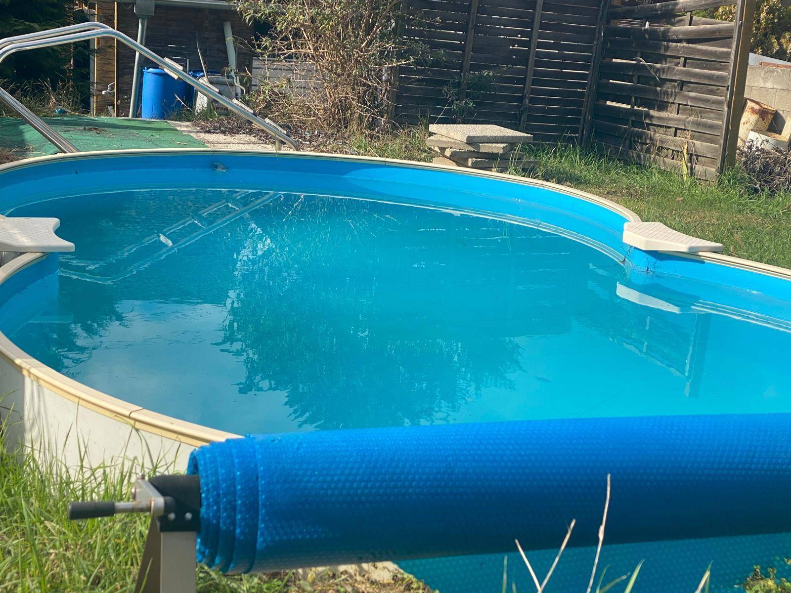 Aufstellpool im Garten mit blauer Abdeckung und umgebender Rasenfläche.