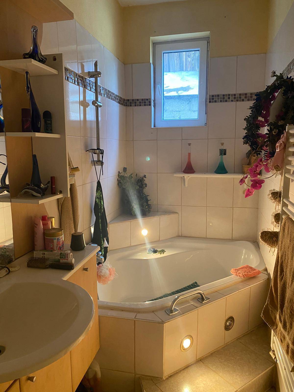 Badezimmer mit Eckbadewanne, Waschbecken und Fenster, hell gefliest.