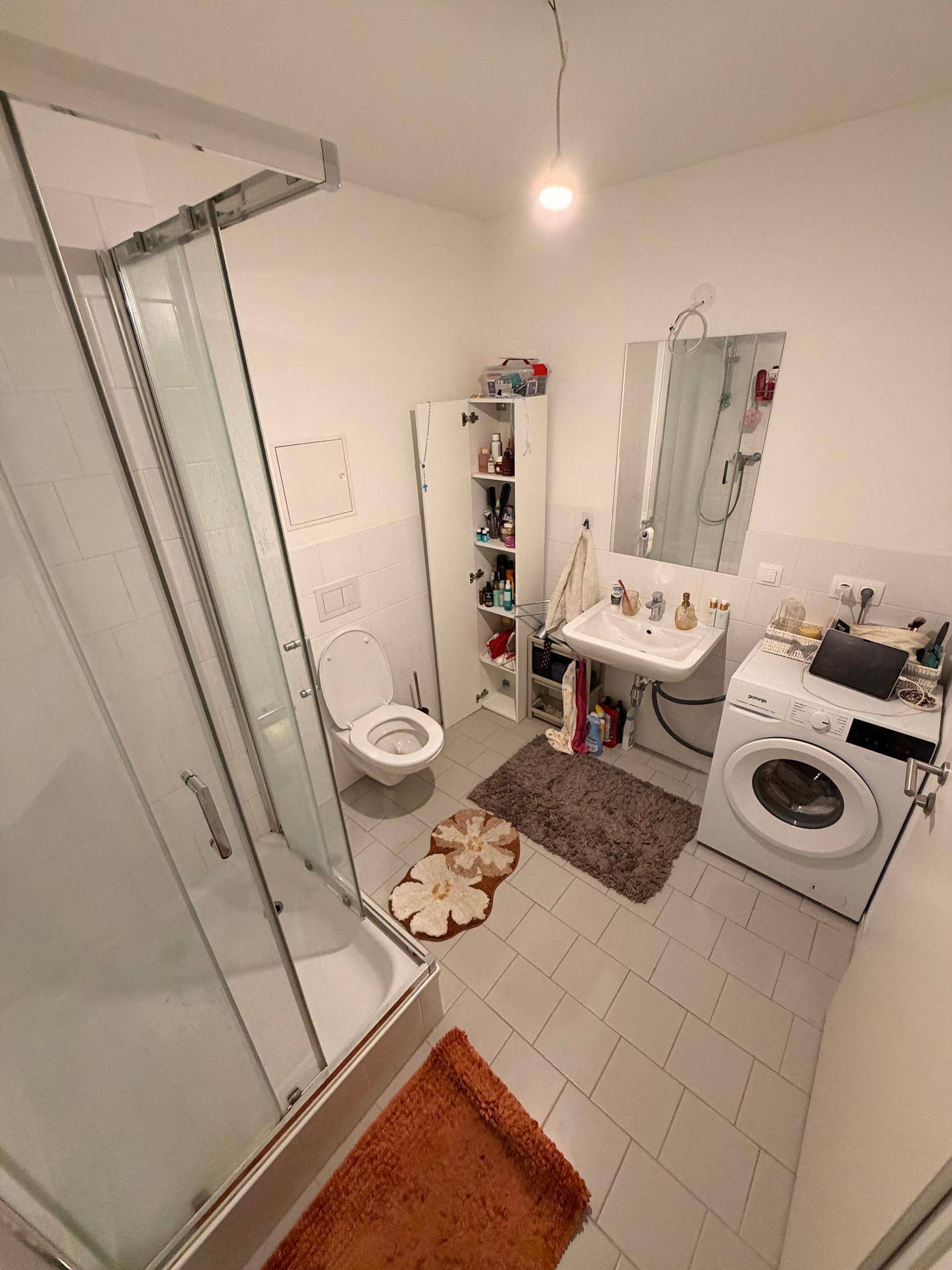 Funktionales Badezimmer mit Duschkabine, WC, Waschbecken und Waschmaschine.