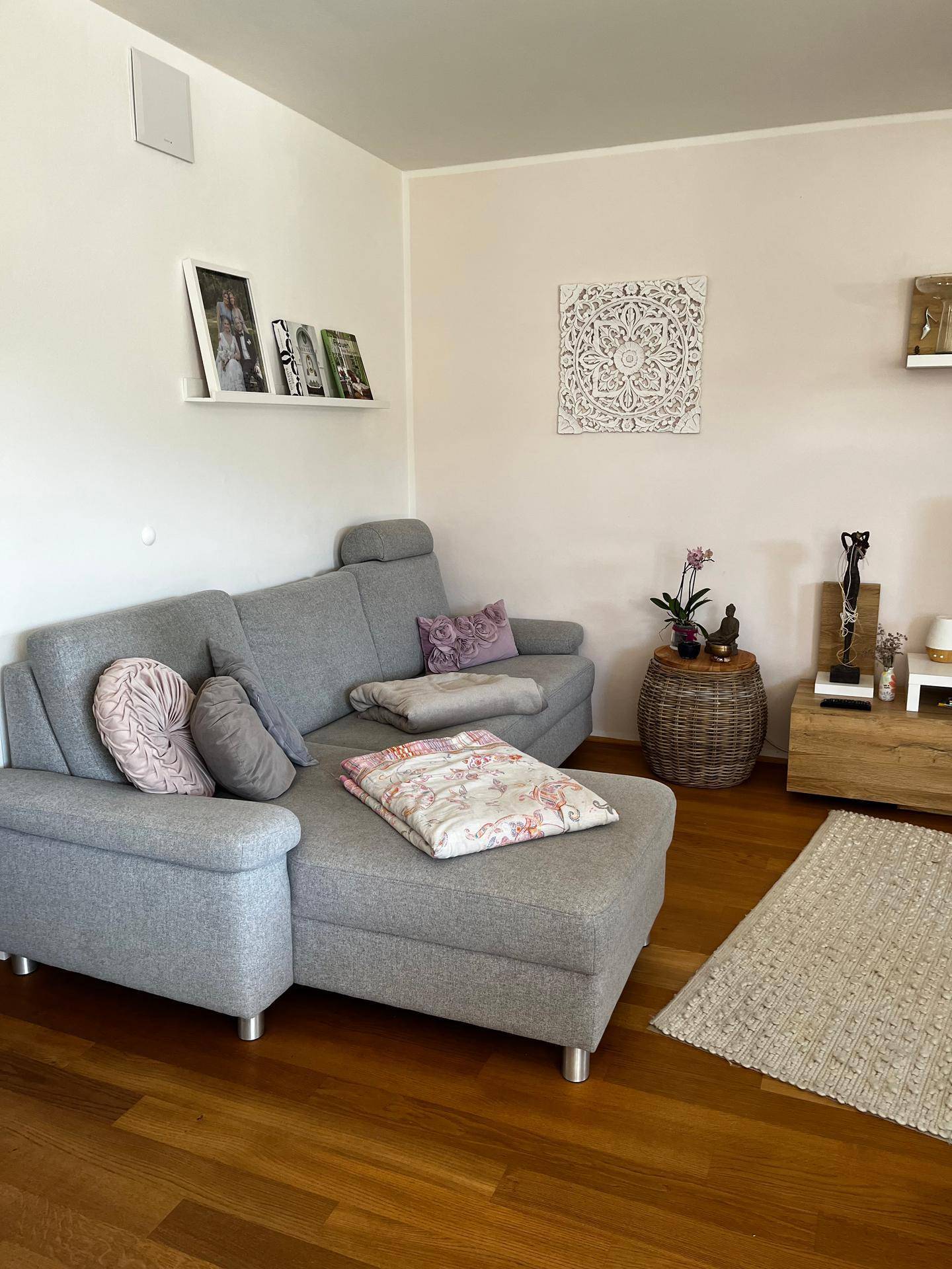 Gemütliches Wohnzimmer mit grauem Ecksofa, Holzboden und dekorativen Wandelementen.