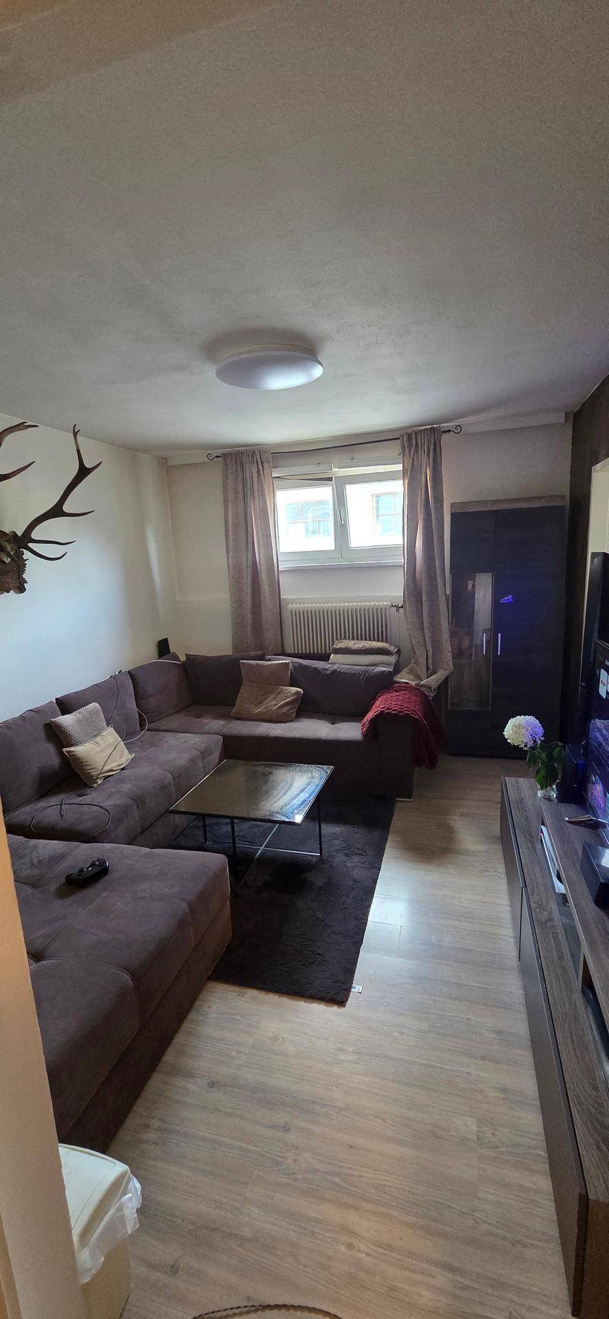 Geräumiges Wohnzimmer mit großem Ecksofa, Fernseher und Fenster.