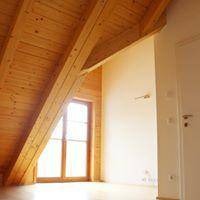 Heller Raum mit schräger Holzdecke, Holzbalken und großem Fenster für viel Tageslicht.