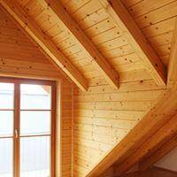 Nahaufnahme einer schrägen Holzdecke mit sichtbaren Balken und einem Fenster.