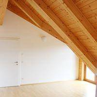 Heller Innenraum mit schräger Holzdecke, Holzbalken und hellem Holzfußboden.